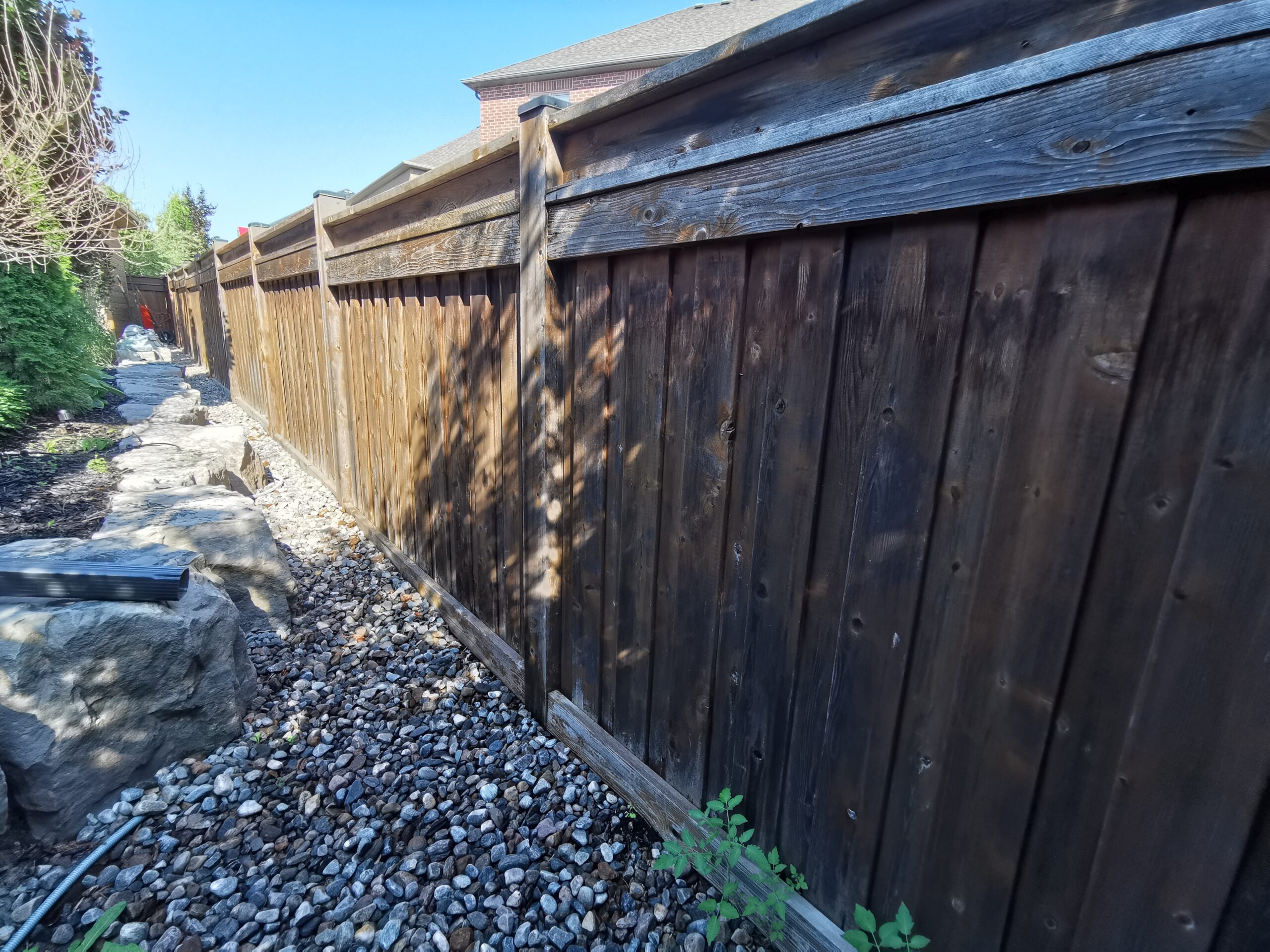 Exterior view of a house in, Vaughan, showing an unstained wooden fence and an unpainted door. The wooden fence appears weathered, and the door is prepared for painting
