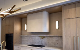 A full shot of a kitchen featuring a range hood and surrounding wall finished in a soft beige microcement. The seamless application eliminates crevices, making it highly hygienic and easy to clean. This finish is sealed for stain-resistance, making it an ideal choice for high-traffic food preparation areas in luxury custom homes.