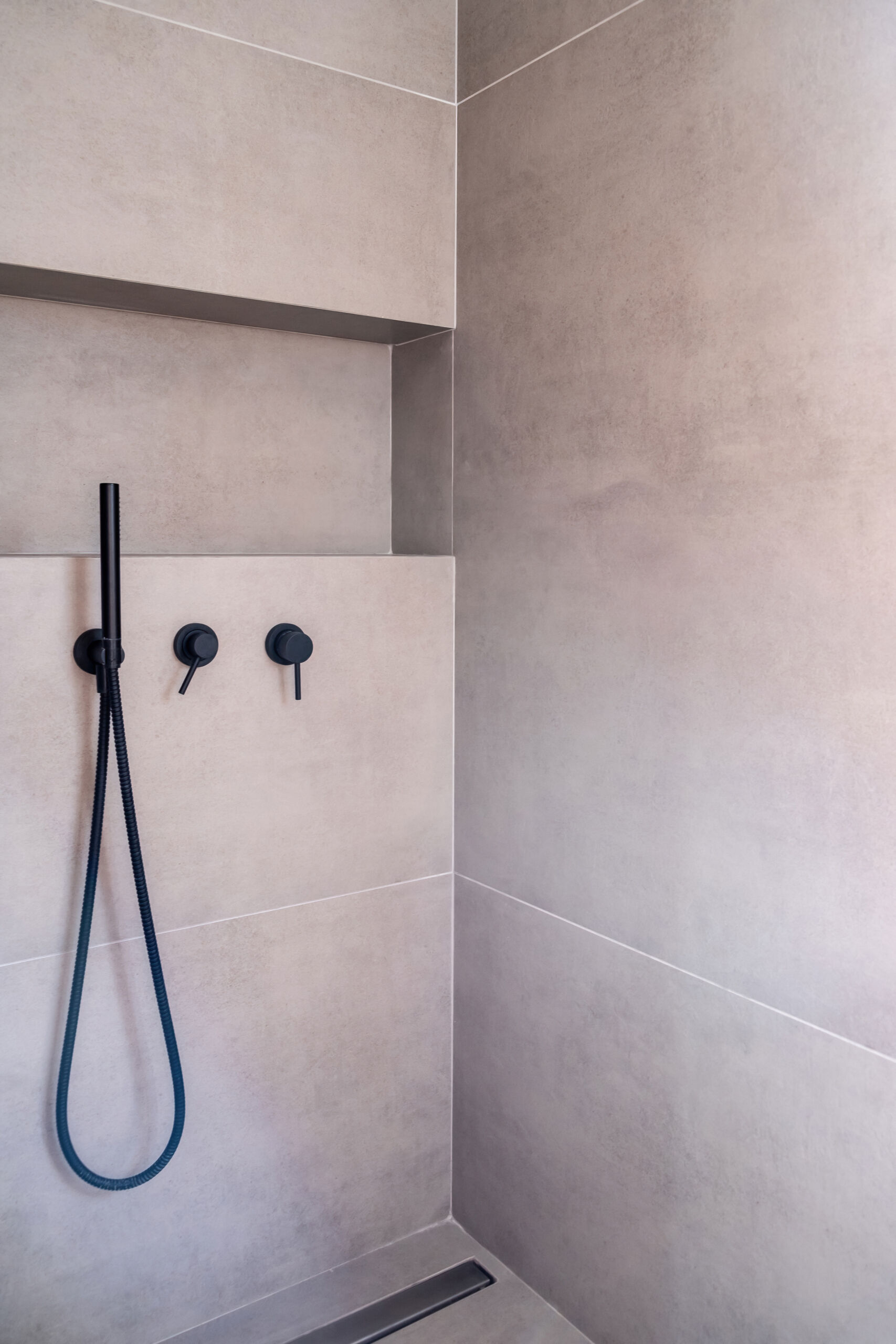 Modern bathroom interior with hand shower faucets black color, on grey ceramic tile wall background Porcelain Slabs vs. Microcement in Modern Toronto Bathrooms