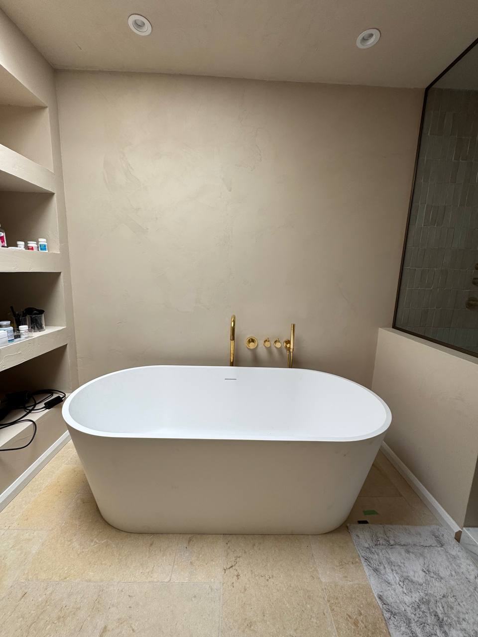 A view of a modern bathroom with a seamless, light-colored microcement finish on the walls and ceiling, featuring custom niches and a skylight.