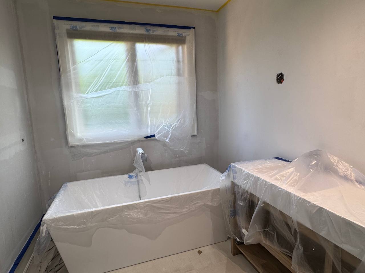 Bare bathroom walls before limewash application, with freestanding tub and window overlooking trees.