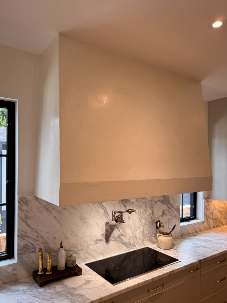 A finished kitchen hood with a smooth, off-white Marmorino Venetian plaster surface and a subtle sheen.