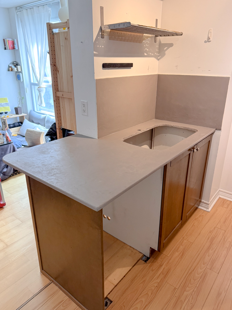 Microcement-kitchen-renovation-microcement-backsplash-microcement-countertop-yorkville,-bloor-2 A newly renovated kitchen featuring a seamless, light gray microcement finish on the countertops and backsplash, giving the space a modern and minimalist look.