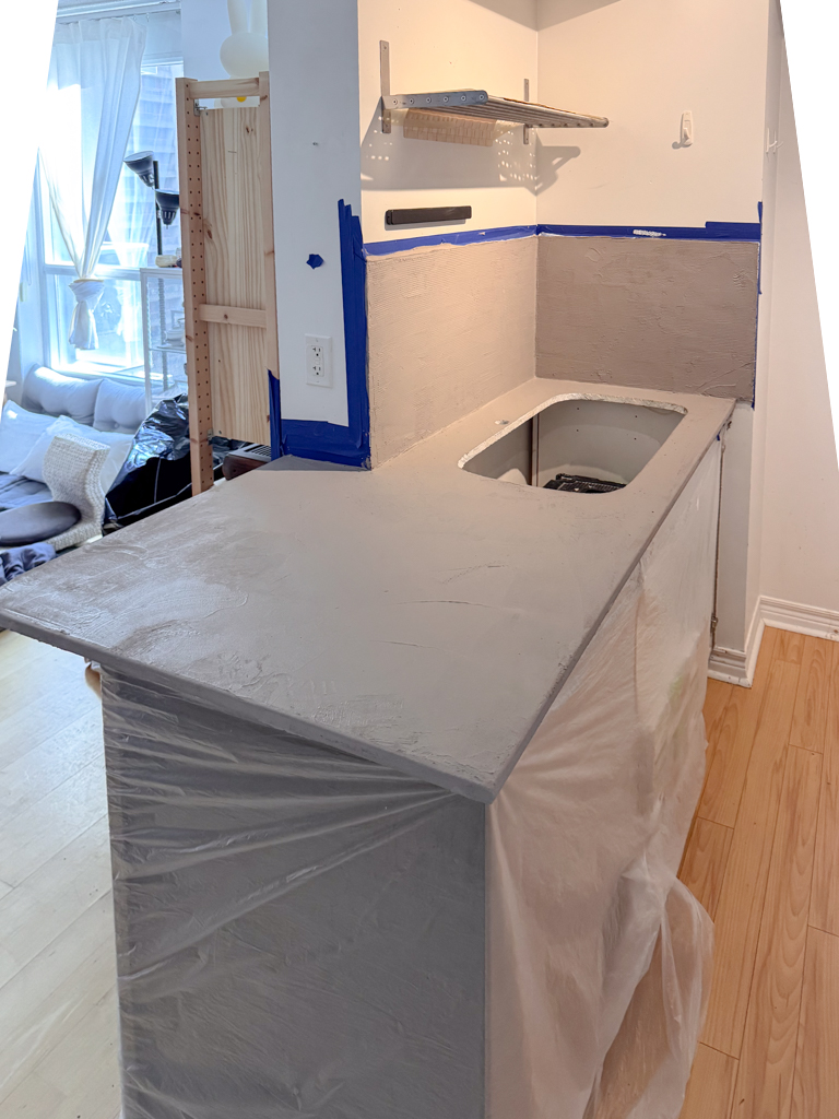 An artisan applying the first layer of gray microcement to a kitchen countertop using a trowel, showing the start of the new seamless finish.