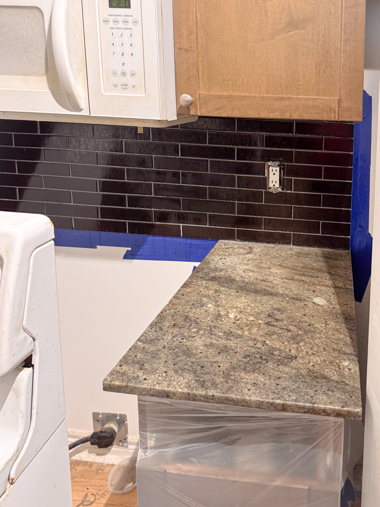 Microcement-kitchen-renovation-microcement-backsplash-microcement-countertop-yorkville,-bloor-8 A worn kitchen with existing countertops and a tiled backsplash, showing visible grout lines and signs of age before renovation.