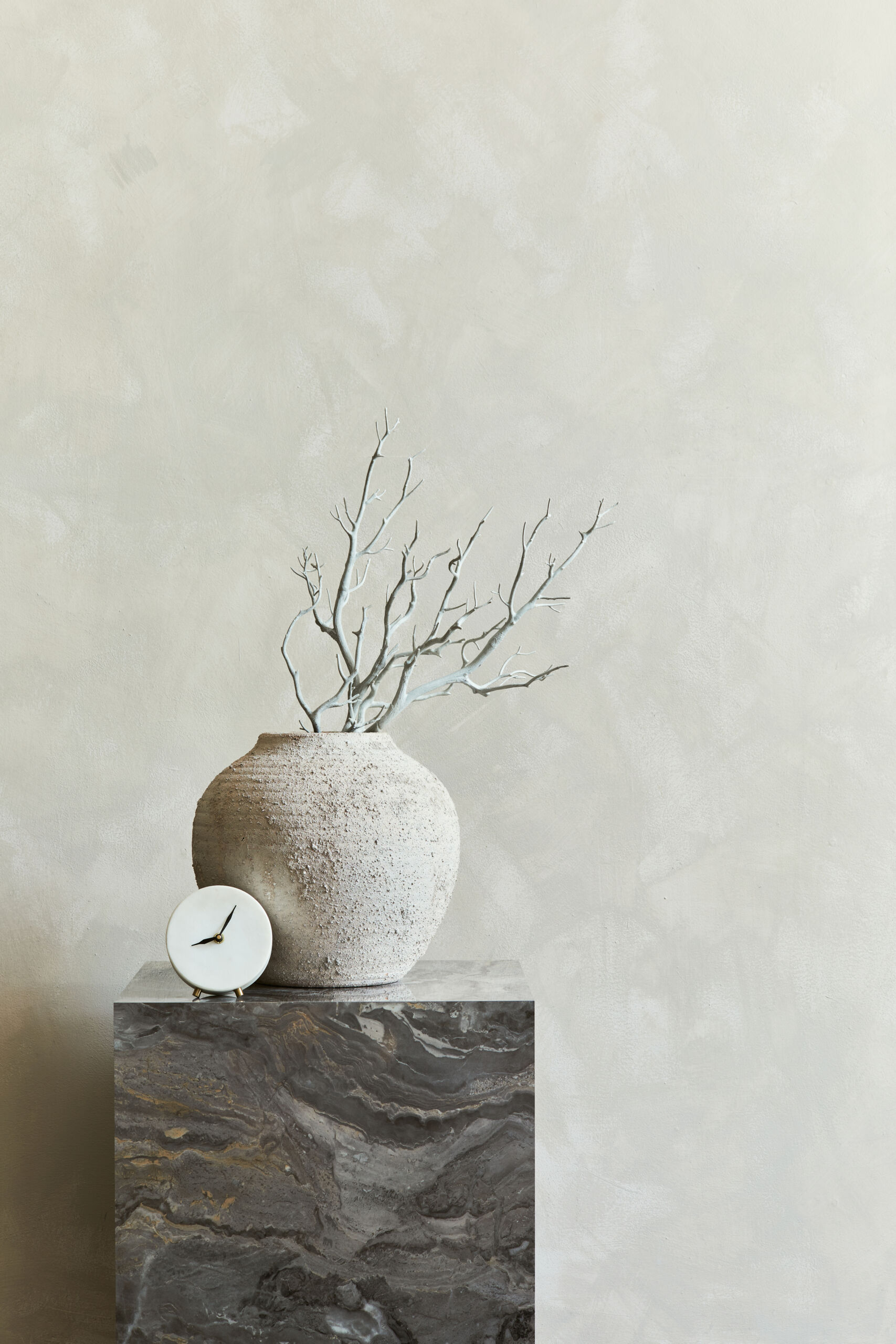Elegant interior composition with marble cube coffee table and stylish personal accessories and vase. Elegant Japandi style living room featuring stone grey plastered walls, a low marble cube coffee table, and minimalist accessories.
