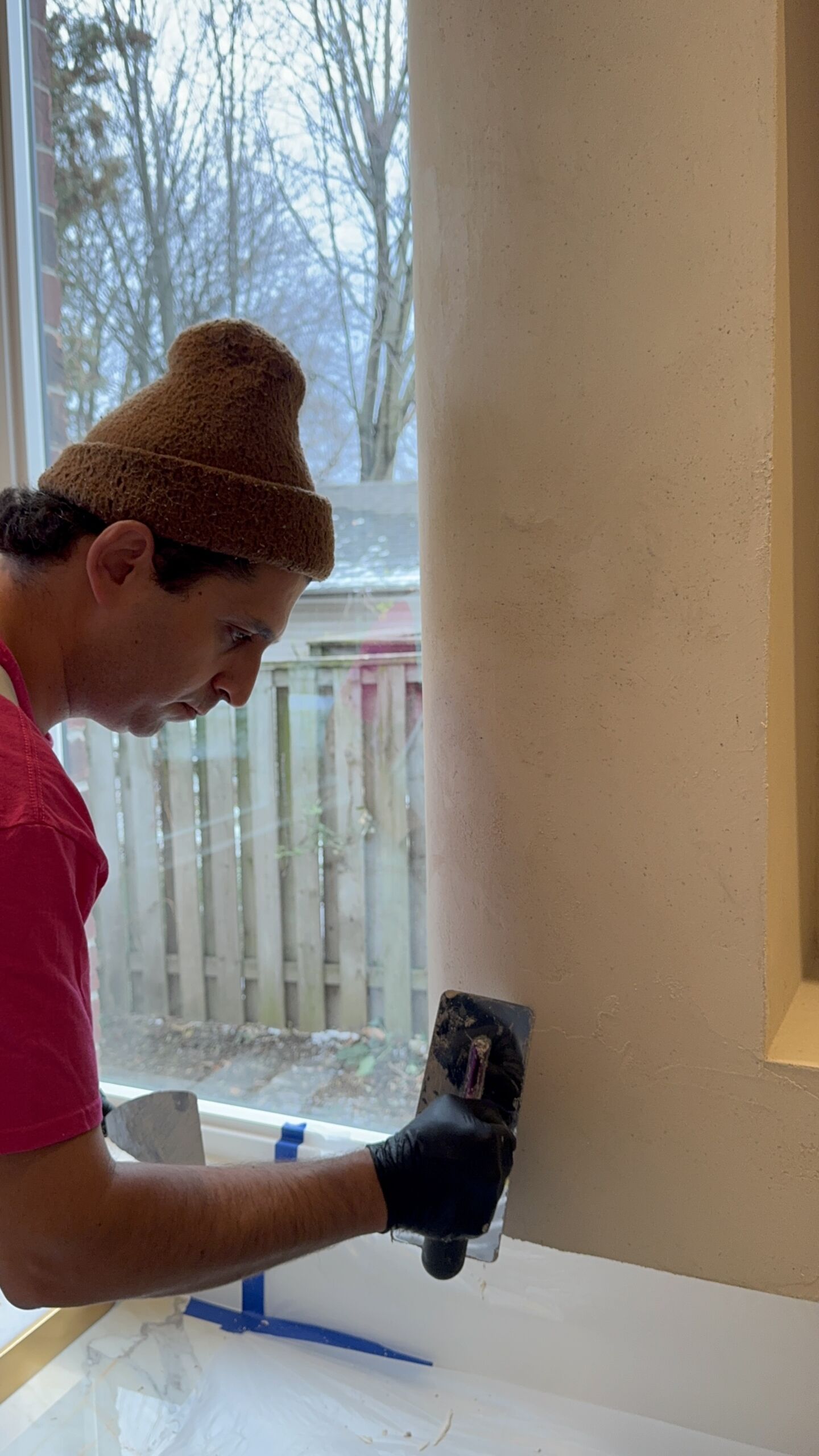 microcement-infused-with-stone-flakes-installation-on-fireplace-in-etobicoke-toronto Skilled artisan applying the second coat of taupe microcement infused with gold and silver mica flakes to a fireplace surround.