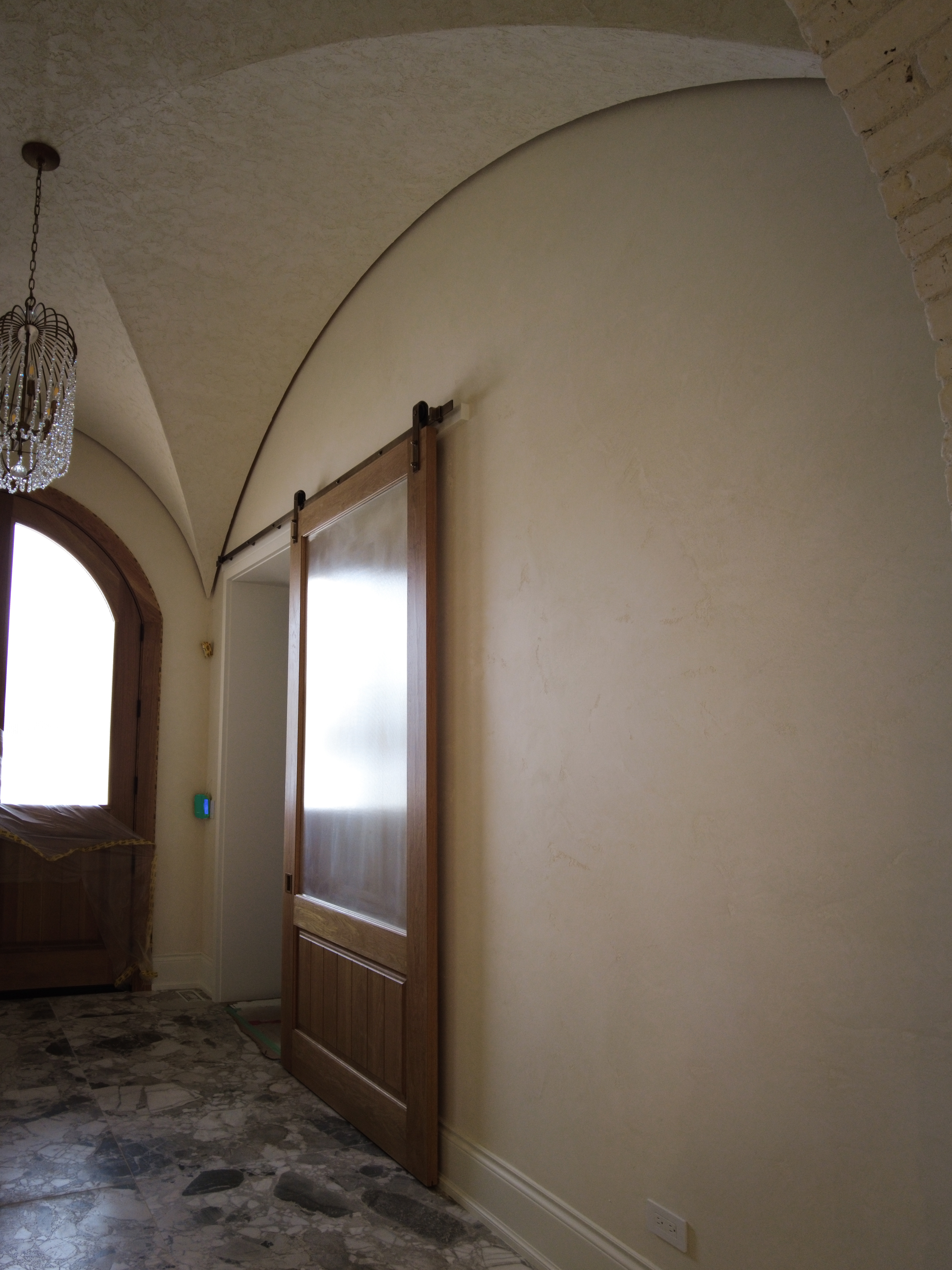 Finished curved foyer ceiling in Kleinburg featuring a rustic, rough-textured Venetian Plaster finish in a soft warm white, contrasting with dark wooden barn sliding doors.