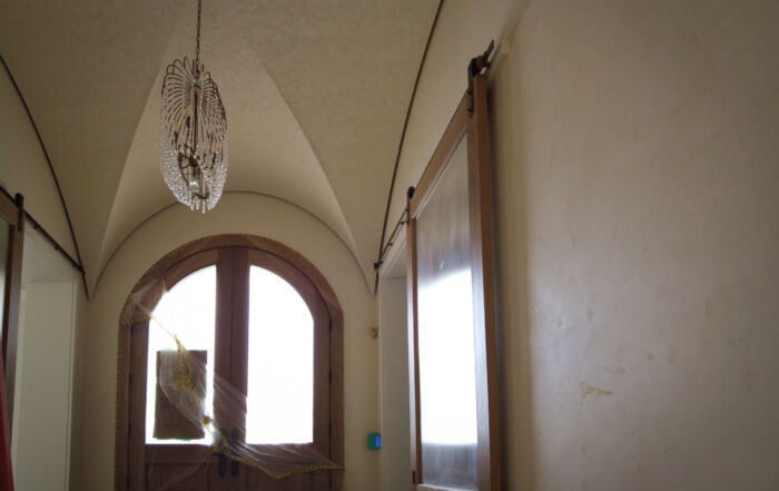 Finished curved foyer ceiling in Kleinburg featuring a rustic, rough-textured Venetian Plaster finish in a soft warm white, contrasting with dark wooden barn sliding doors.