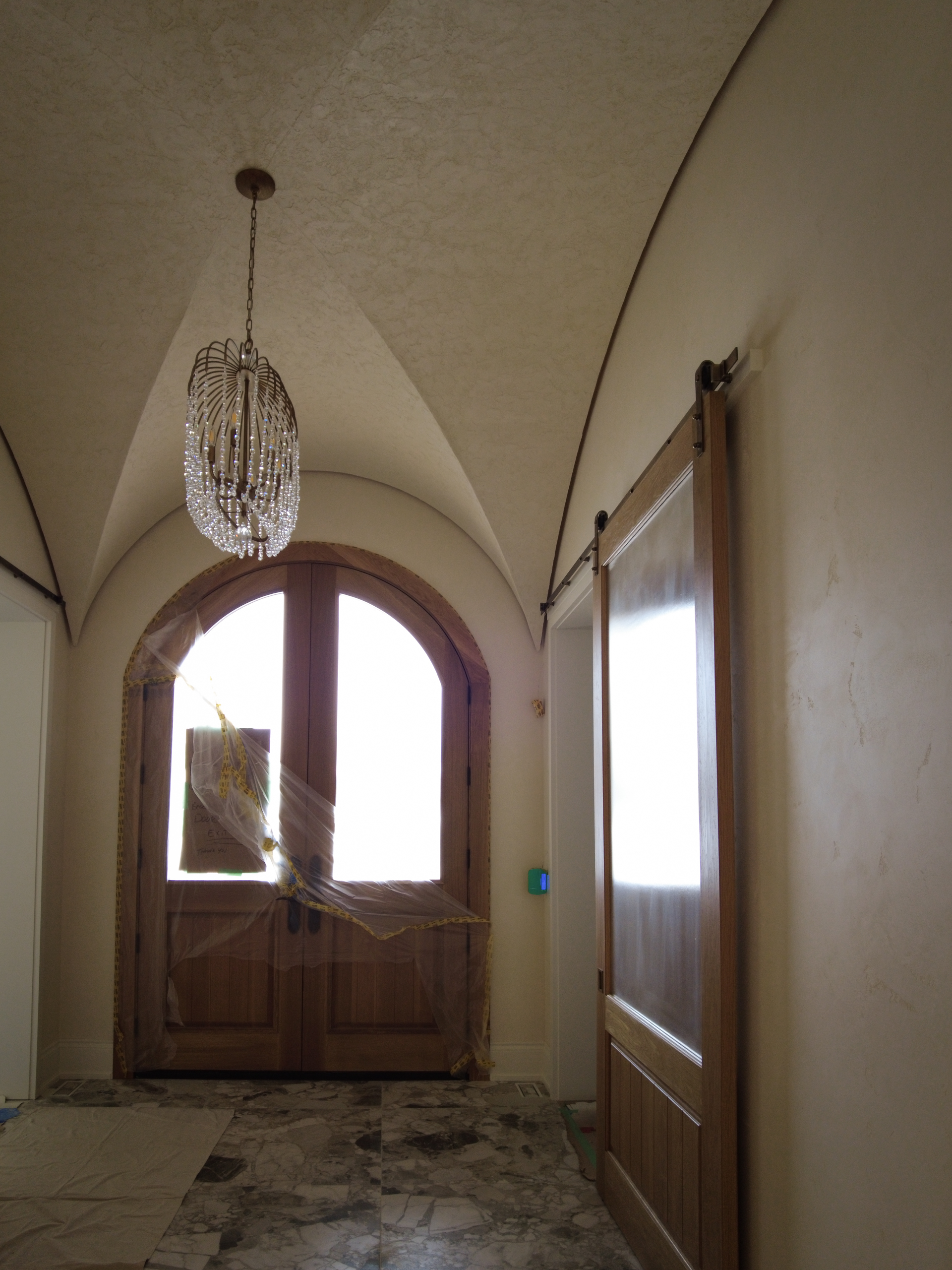 Timeless-Marmorino-Venetian-Plaster-Foyer-Hallway-Kleinburg Finished curved foyer ceiling in Kleinburg featuring a rustic, rough-textured Venetian Plaster finish in a soft warm white, contrasting with dark wooden barn sliding doors.