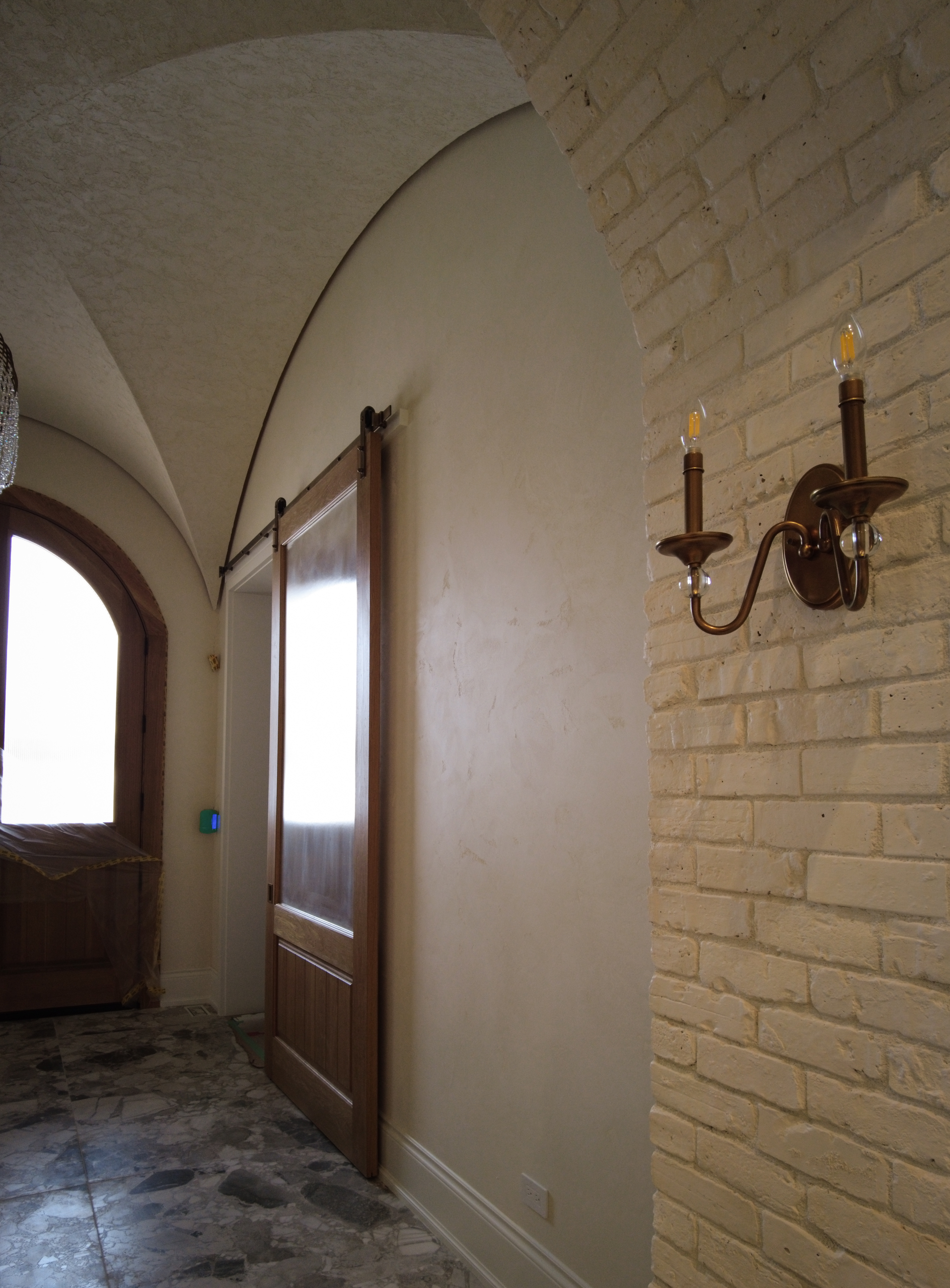 Timeless-Marmorino-Venetian-Plaster-Foyer-Hallway-Kleinburg Finished curved foyer ceiling in Kleinburg featuring a rustic, rough-textured Venetian Plaster finish in a soft warm white, contrasting with dark wooden barn sliding doors.