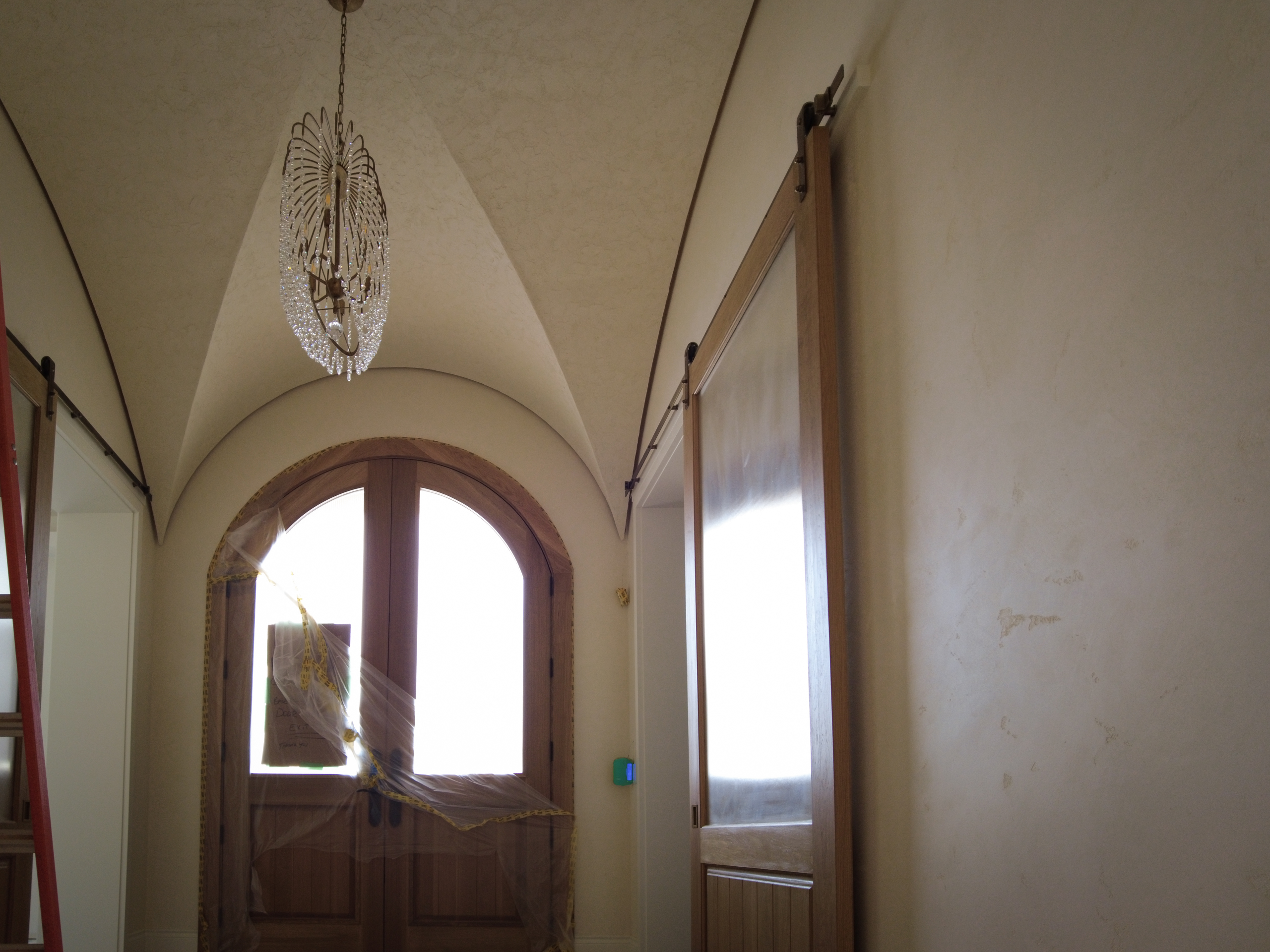 Timeless-Marmorino-Venetian-Plaster-Foyer-Hallway-Kleinburg Finished curved foyer ceiling in Kleinburg featuring a rustic, rough-textured Venetian Plaster finish in a soft warm white, contrasting with dark wooden barn sliding doors.