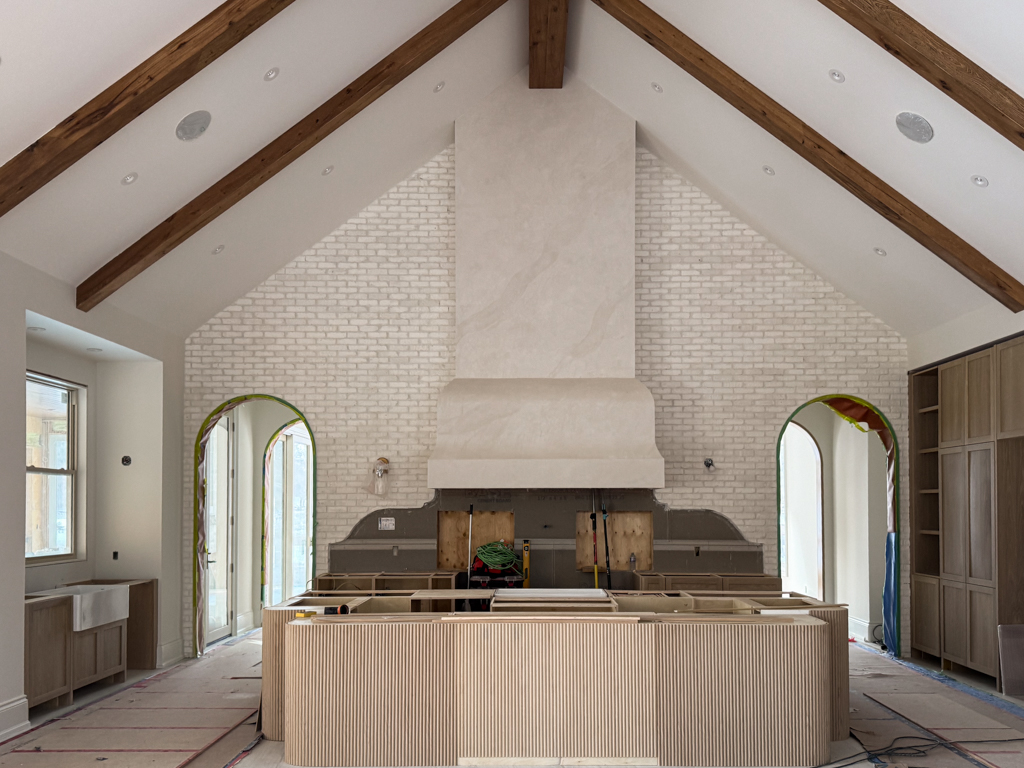 Custom tall kitchen range hood finished in Pearly Venetian Plaster featuring a soft iridescent shimmer, framed by rustic wooden beams in a luxury Kleinburg farmhouse.