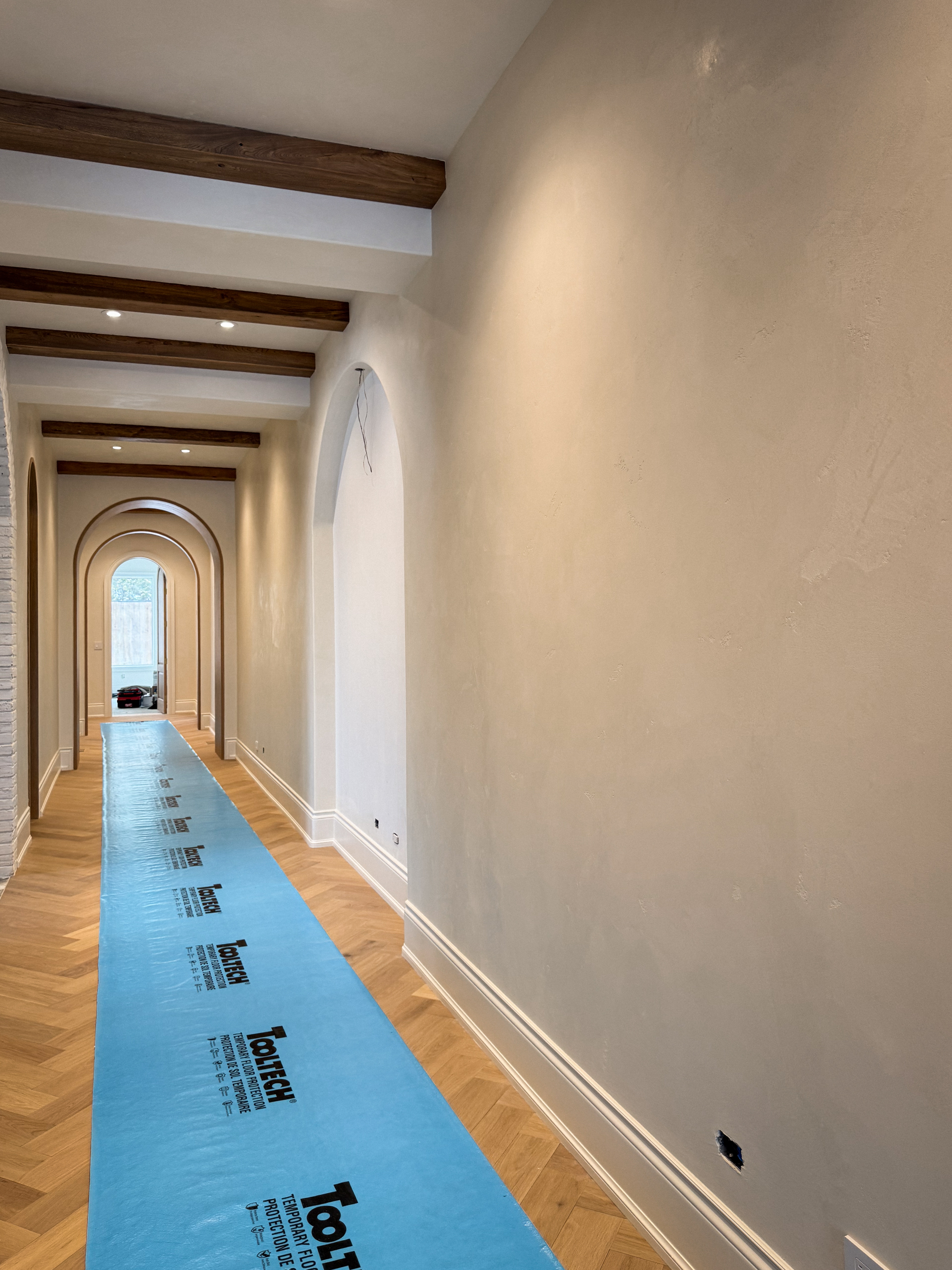 A finished luxury hallway at Kleins Ridge with soft warm white Venetian Plaster walls and ceiling, perfectly integrated with dark walnut beams.