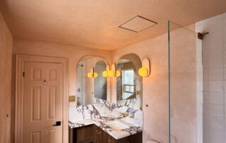 A small, modern bathroom featuring seamless matte Venetian Plaster walls in a warm pinkish-beige tone, creating a soft, cloudy texture that wraps around a minimalist vanity.