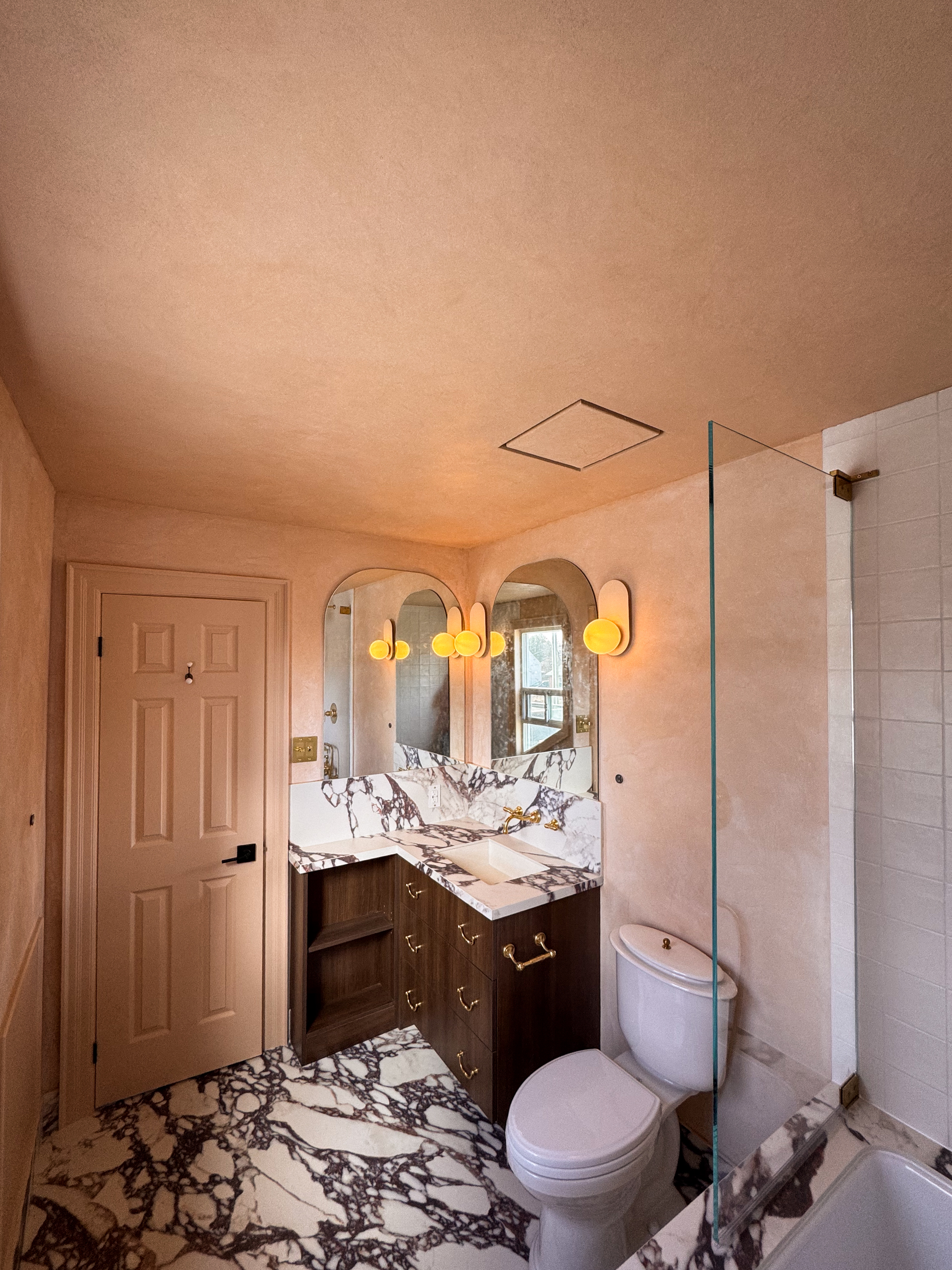A small, modern bathroom featuring seamless matte Venetian Plaster walls in a warm pinkish-beige tone, creating a soft, cloudy texture that wraps around a minimalist vanity.
