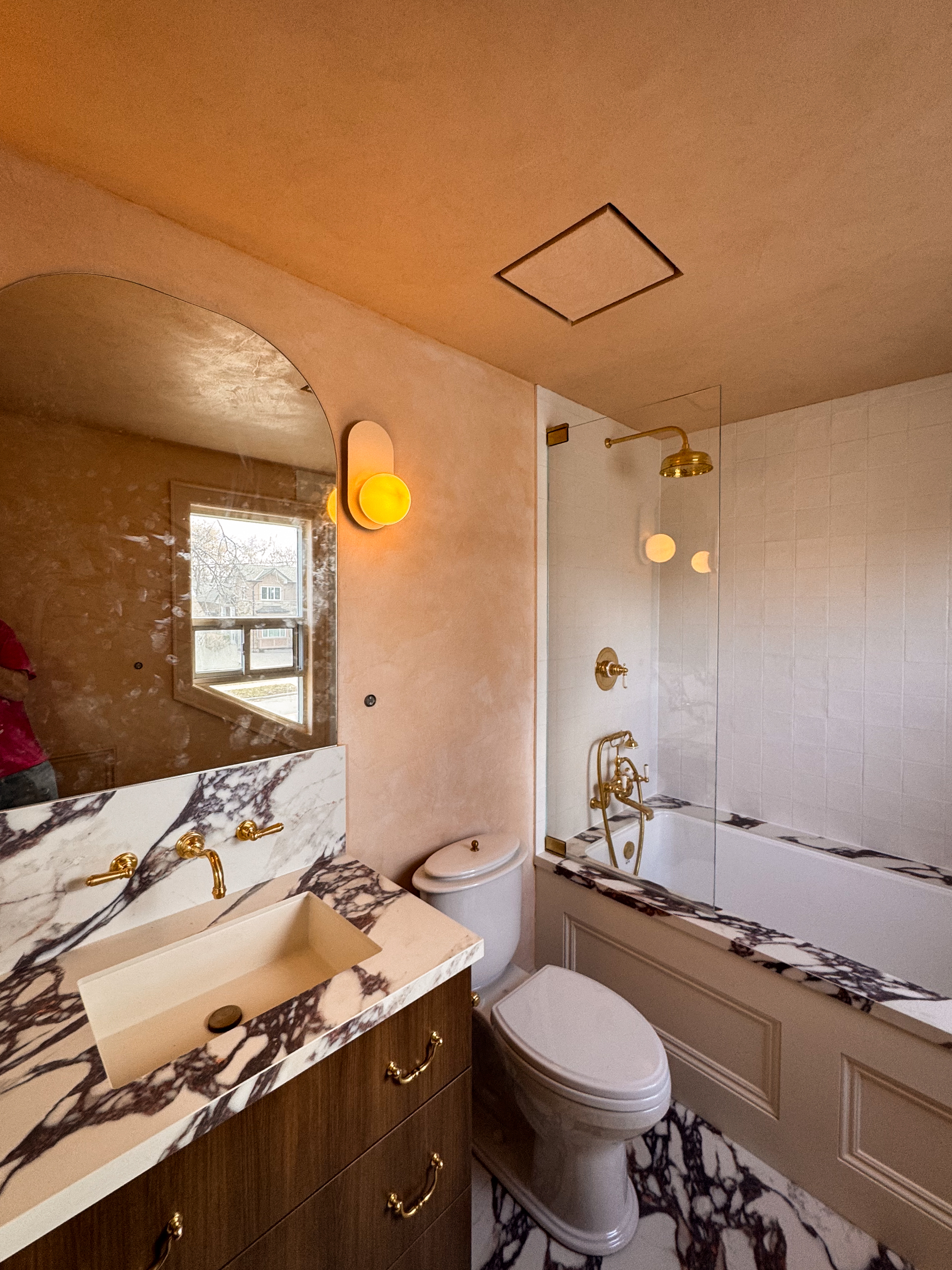 A small, modern bathroom featuring seamless matte Venetian Plaster walls in a warm pinkish-beige tone, creating a soft, cloudy texture that wraps around a minimalist vanity.