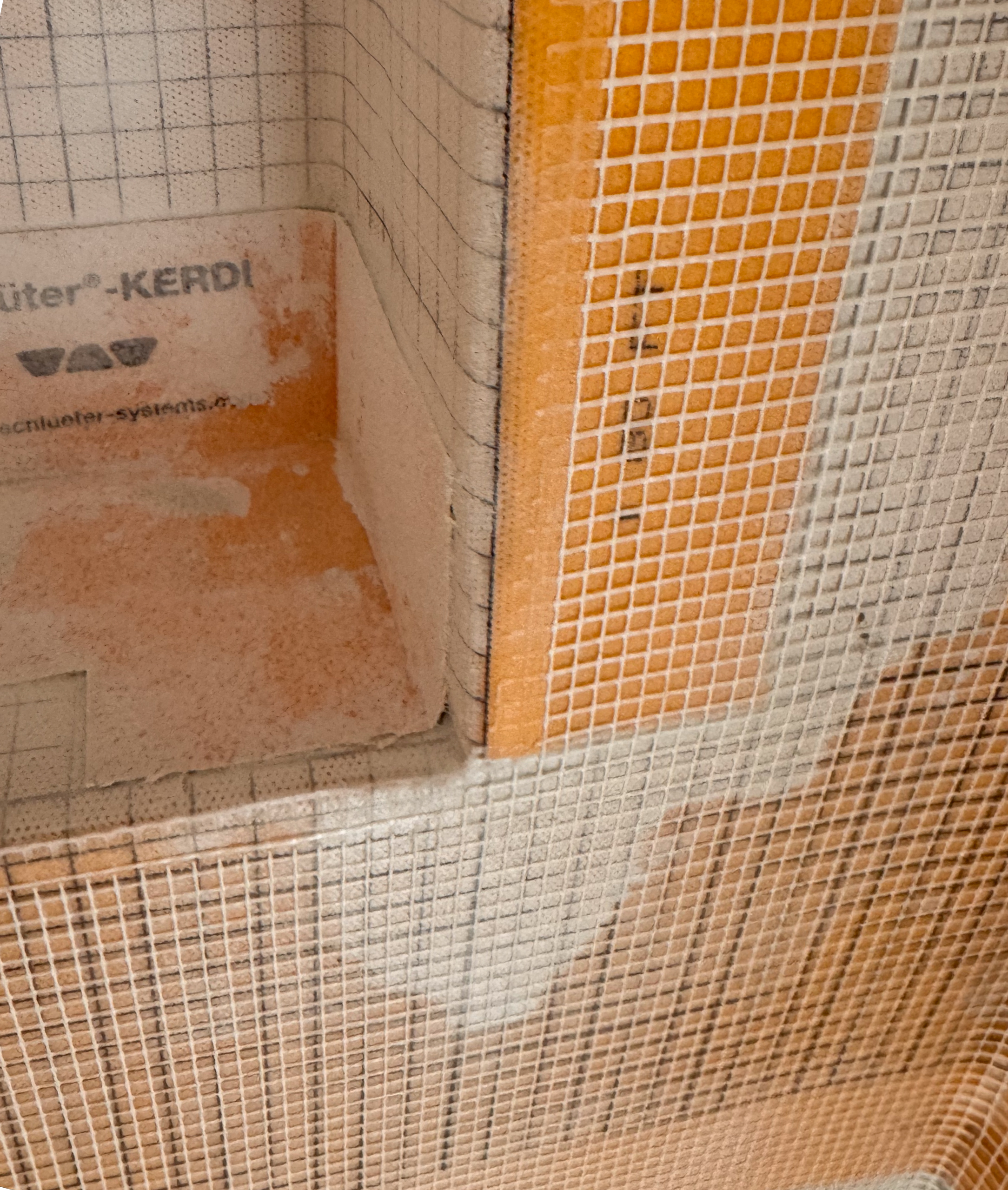 A photo showing a badly prepped shower corner with bunched, overlapping, and loose Schluter waterproofing membrane before microcement application.