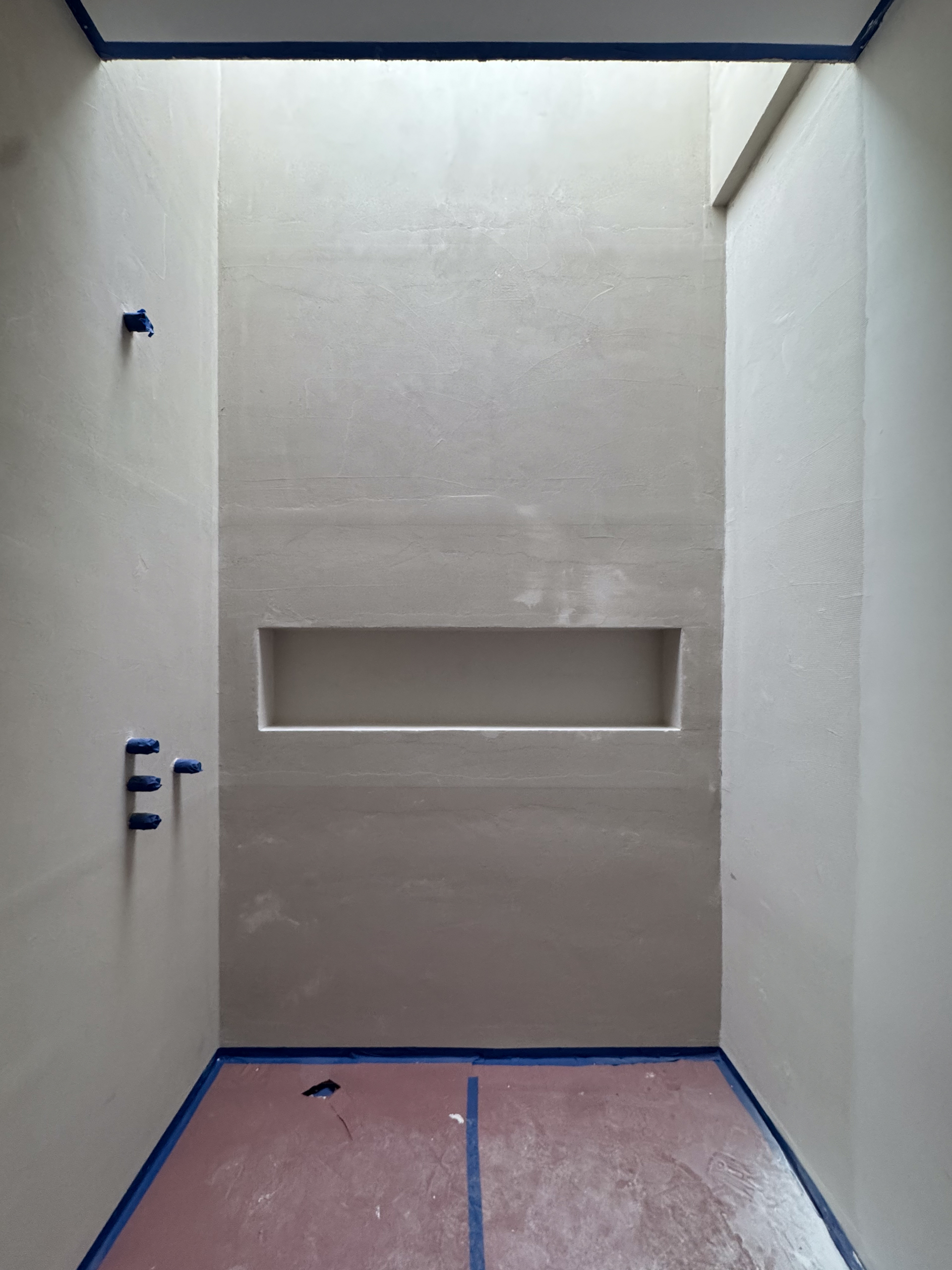 Why Insecure Waterproofing Membranes Cause Microcement Failure A close-up of a microcement wall where the rectangular outlines of the Schluter membrane overlaps are visible through the decorative finish.