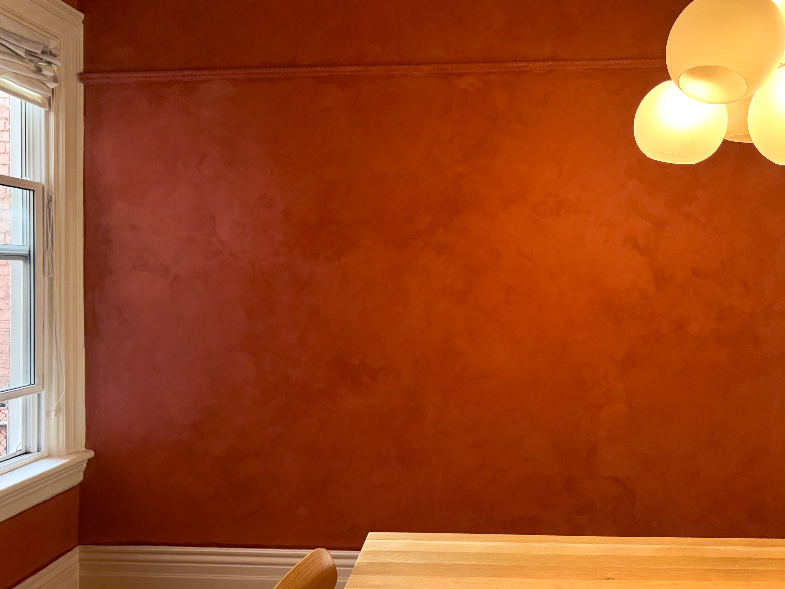 A restored Toronto Victorian living room featuring deep terracotta limewash walls, intricate white crown moldings, and walnut wood furniture, inspired by timeless interiors.