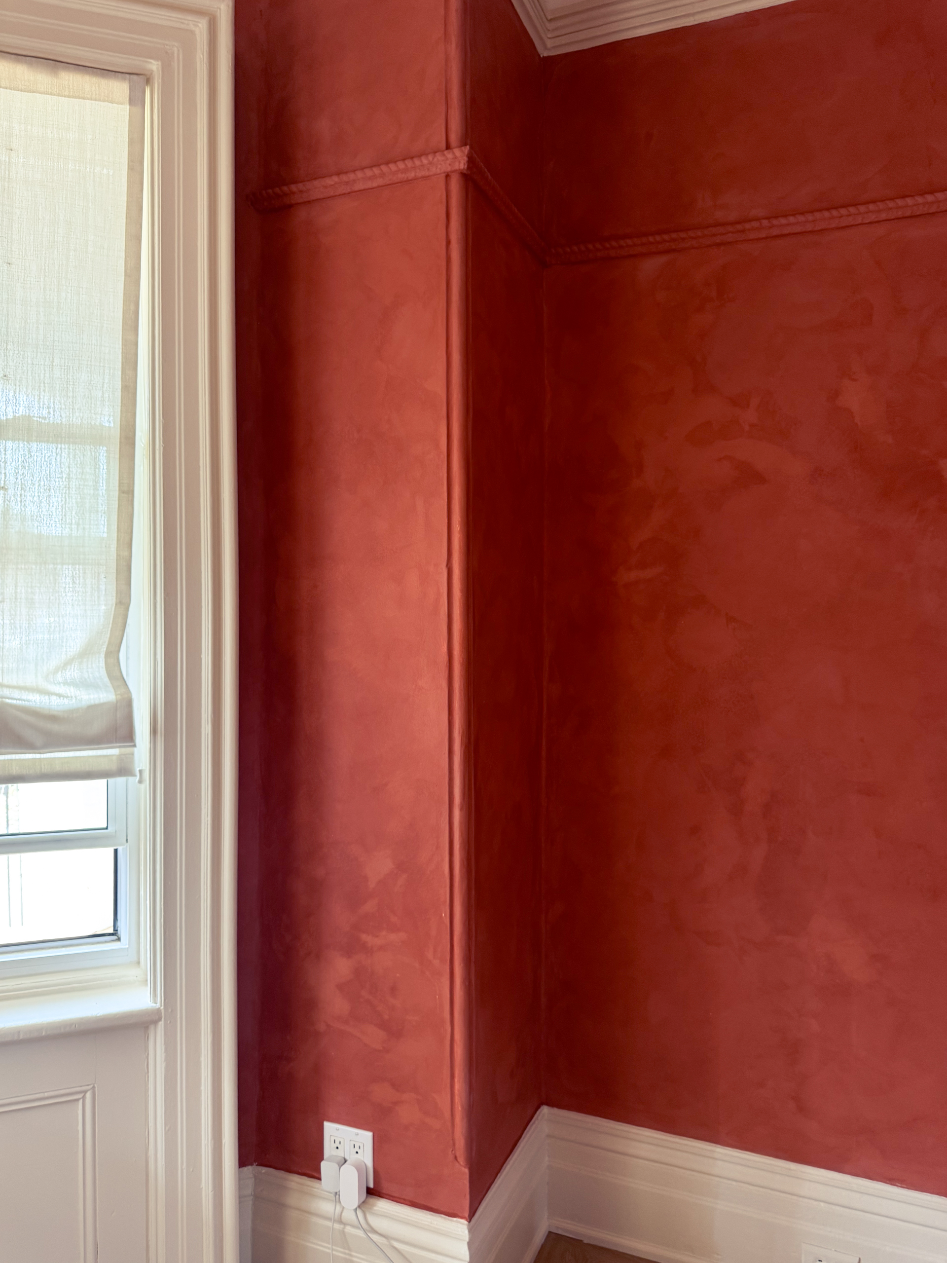 A restored Toronto Victorian living room featuring deep terracotta limewash walls, intricate white crown moldings, and walnut wood furniture, inspired by timeless interiors.