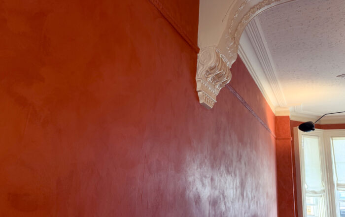 A restored Toronto Victorian living room featuring deep terracotta limewash walls, intricate white crown moldings, and walnut wood furniture, inspired by timeless interiors.
