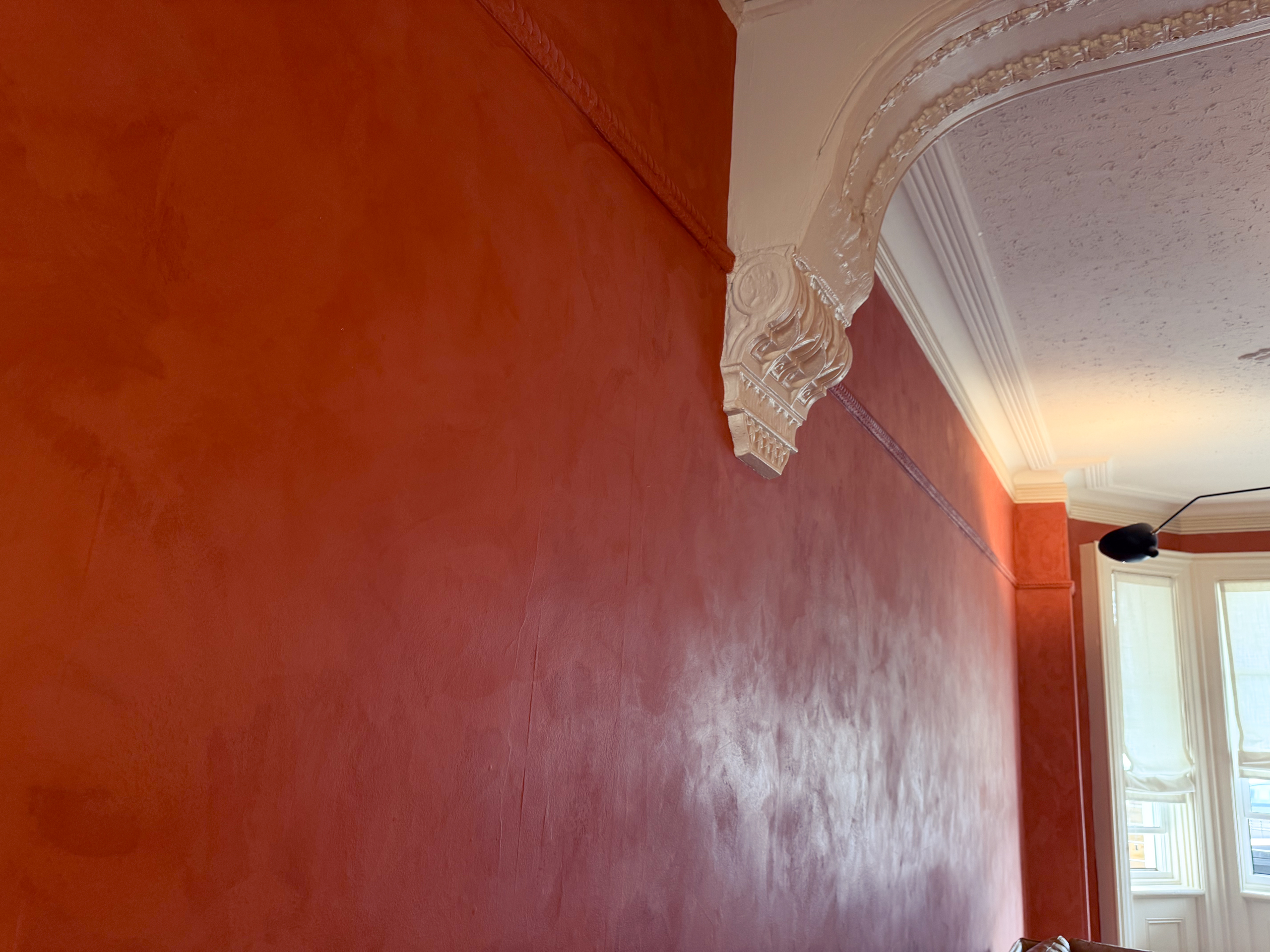 A restored Toronto Victorian living room featuring deep terracotta limewash walls, intricate white crown moldings, and walnut wood furniture, inspired by timeless interiors.