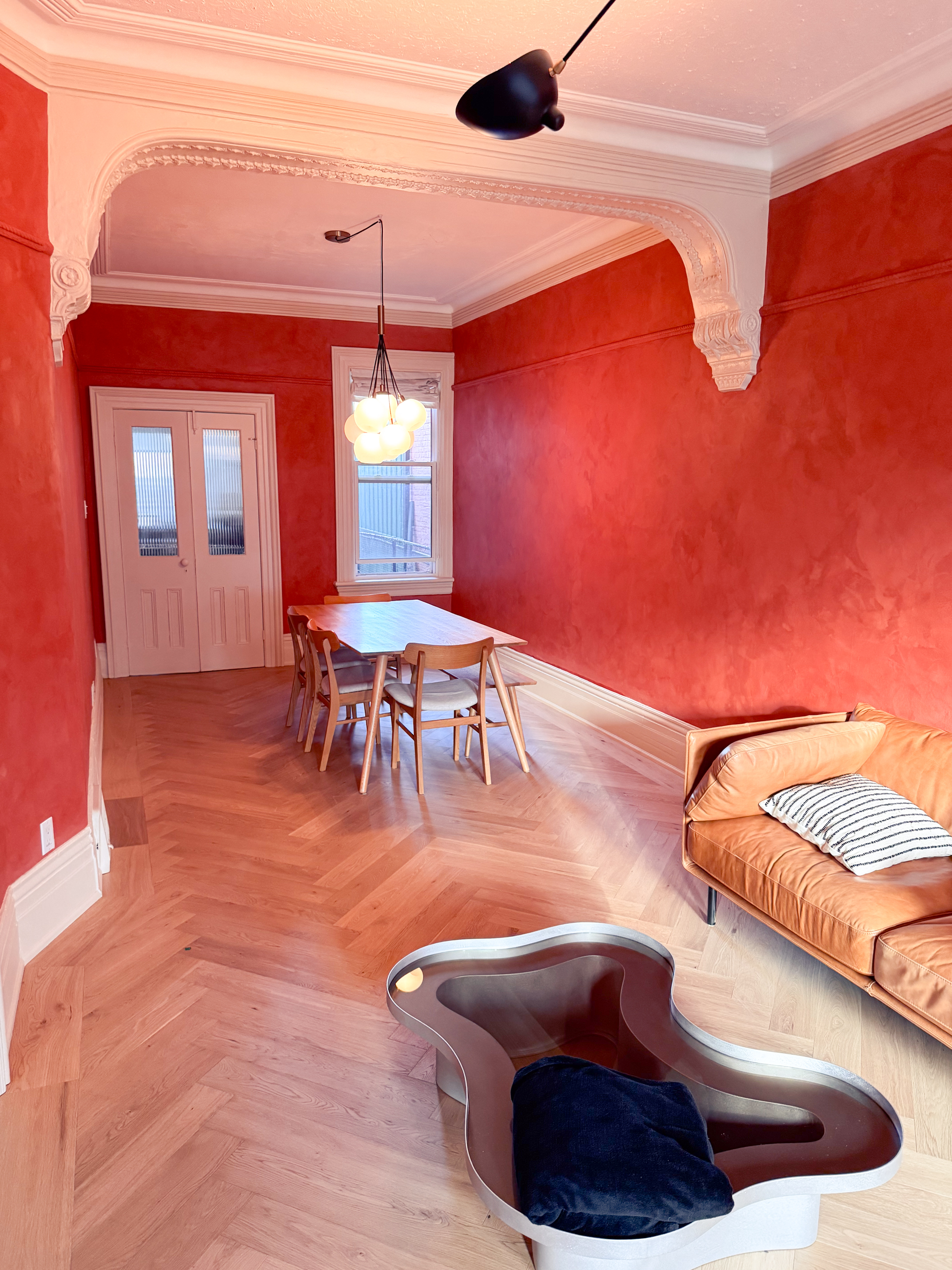 A restored Toronto Victorian living room featuring deep terracotta limewash walls, intricate white crown moldings, and walnut wood furniture, inspired by timeless interiors.