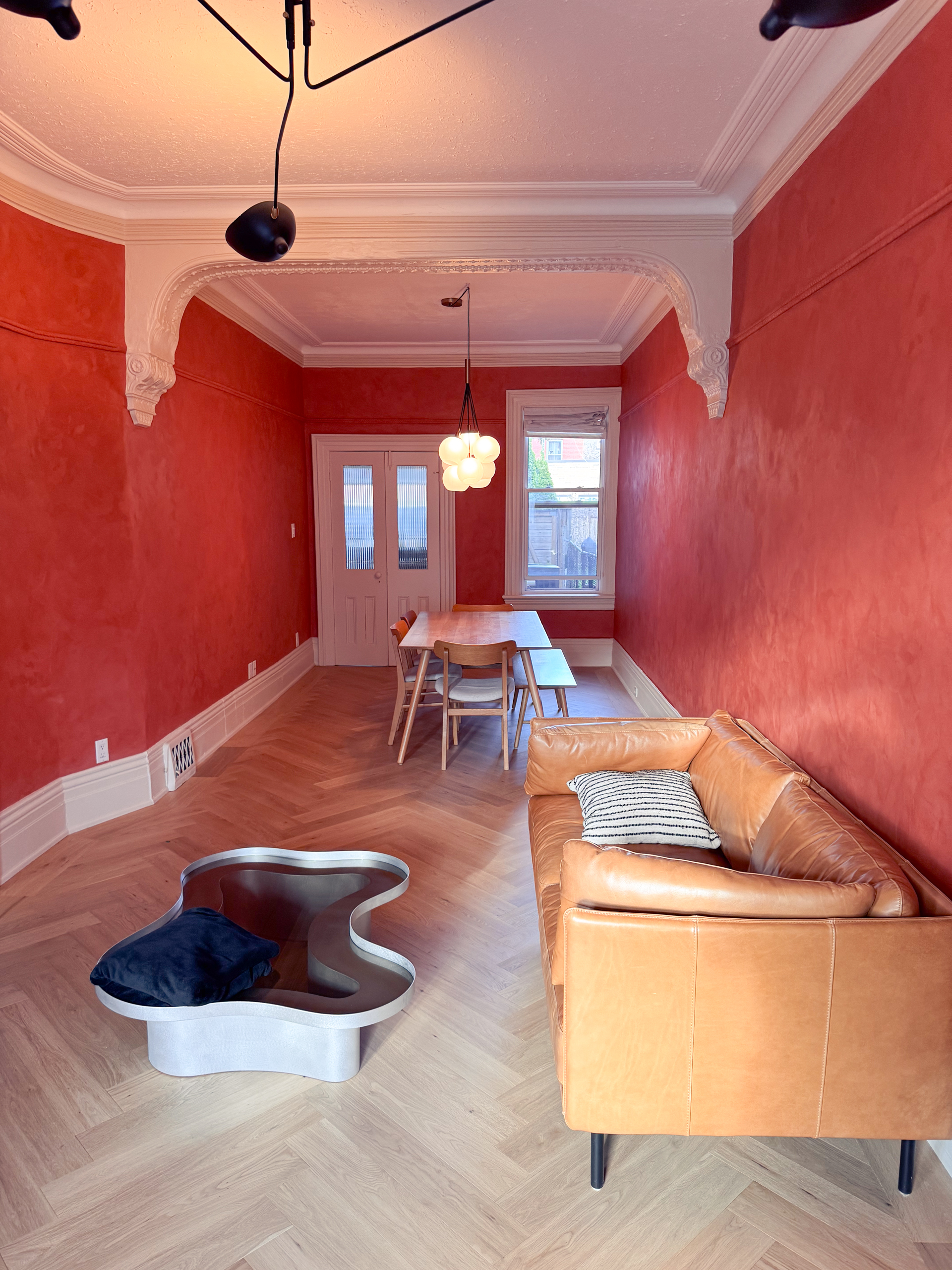 A restored Toronto Victorian living room featuring deep terracotta limewash walls, intricate white crown moldings, and walnut wood furniture, inspired by timeless interiors.