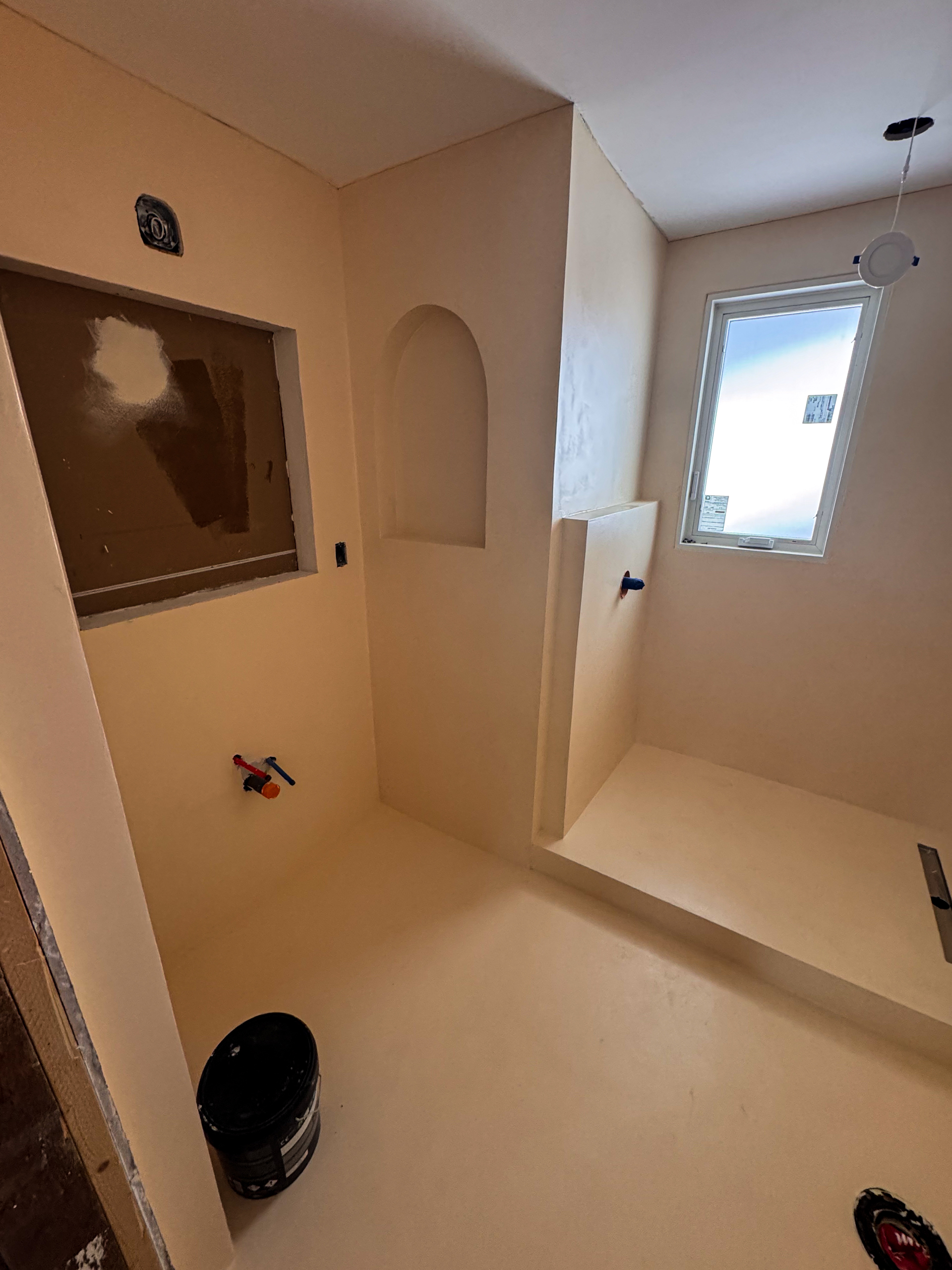 Grout-free modern walk-in shower wrapped in soft peach microcement walls and floors with minimalist brass fixtures in a Leslieville home.