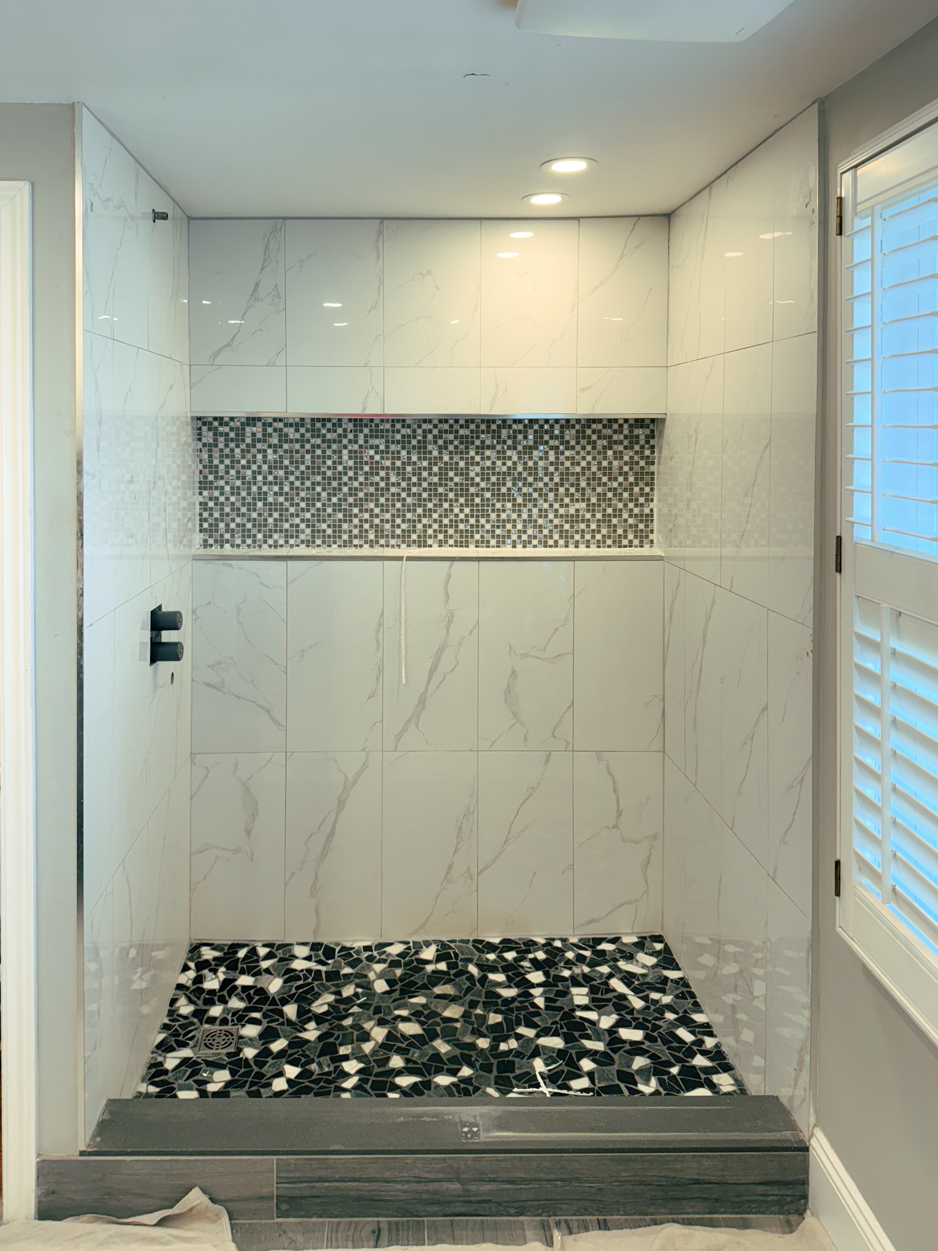 Dated bathroom shower walls and floor tiles with a built-in niche before a microcement installation in Toronto.