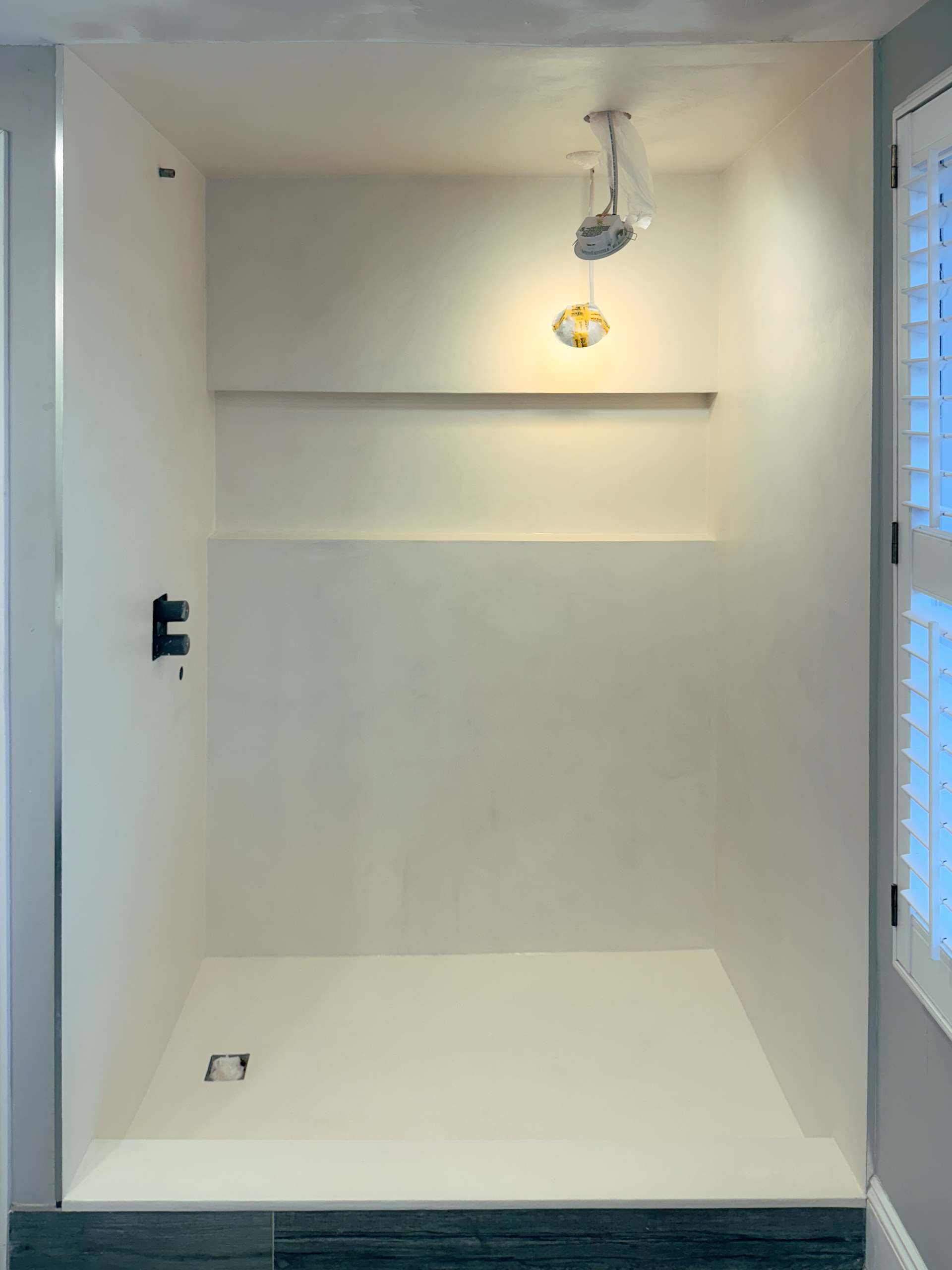 After photo of a seamless warm creamy white microcement shower with wrapped walls, floor, and a clean built-in niche in Toronto.