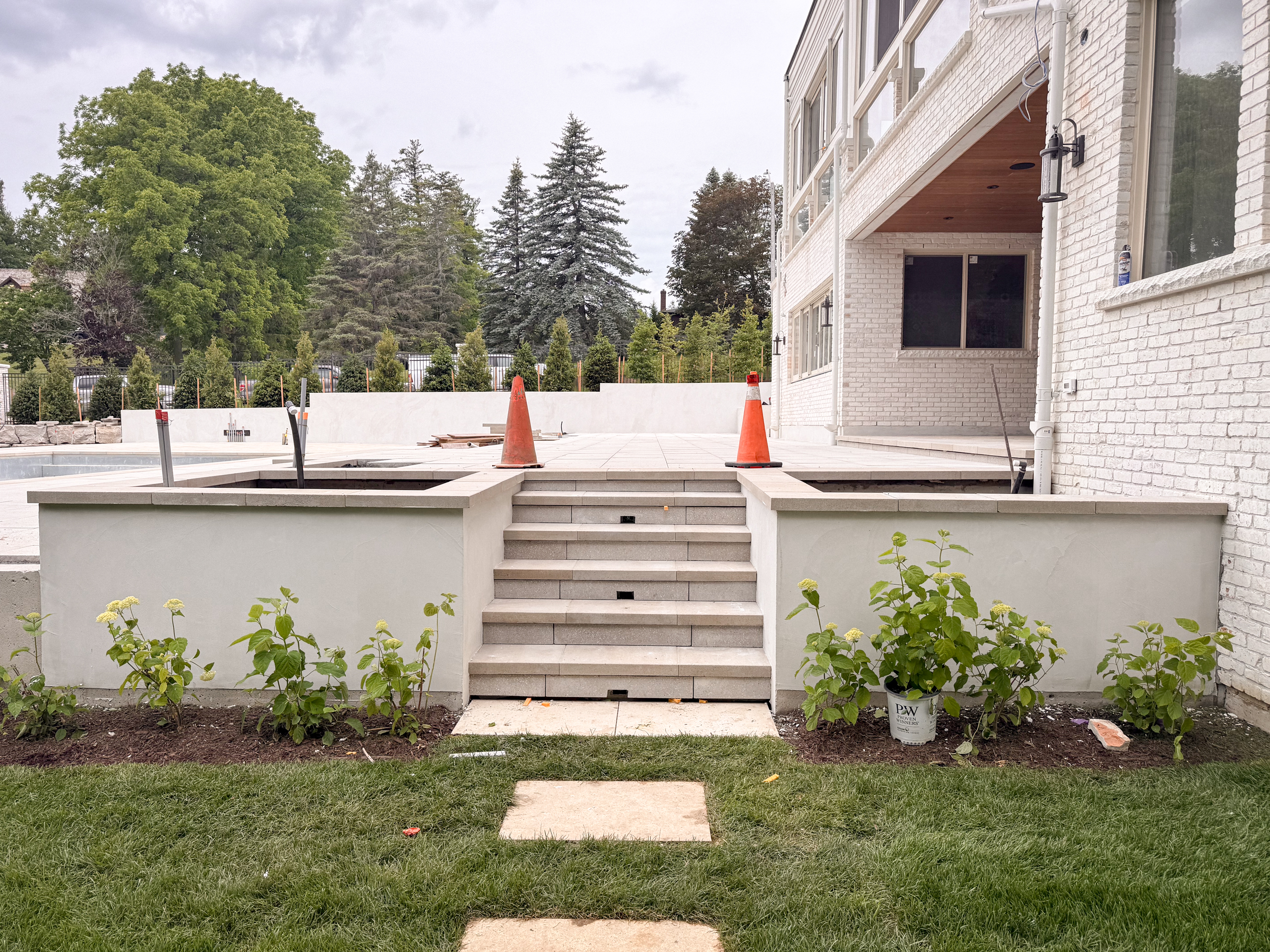 white-exterior-microcement-planters-kleinburg-toronto-2 Close-up of a modern outdoor garden in Kleinburg featuring vertical planters and architectural facades finished in a seamless, soft grey exterior microcement over a concrete base, surrounded by manicured landscaping.