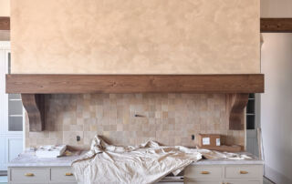An artisan hand-applying a layer of clay-infused limewash with a wide block brush onto a large range hood shroud in a Toronto kitchen.