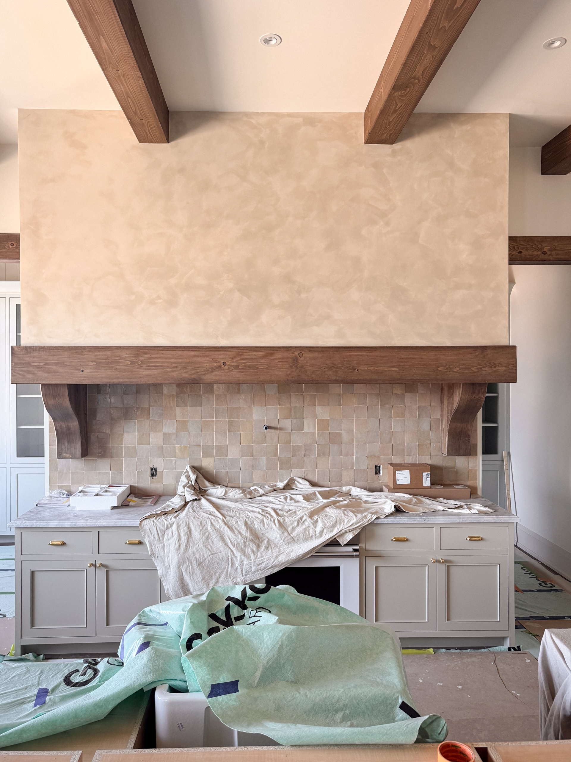 An artisan hand-applying a layer of clay-infused limewash with a wide block brush onto a large range hood shroud in a Toronto kitchen.