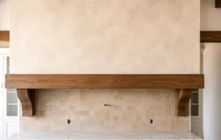 An artisan hand-applying a layer of clay-infused limewash with a wide block brush onto a large range hood shroud in a Toronto kitchen.