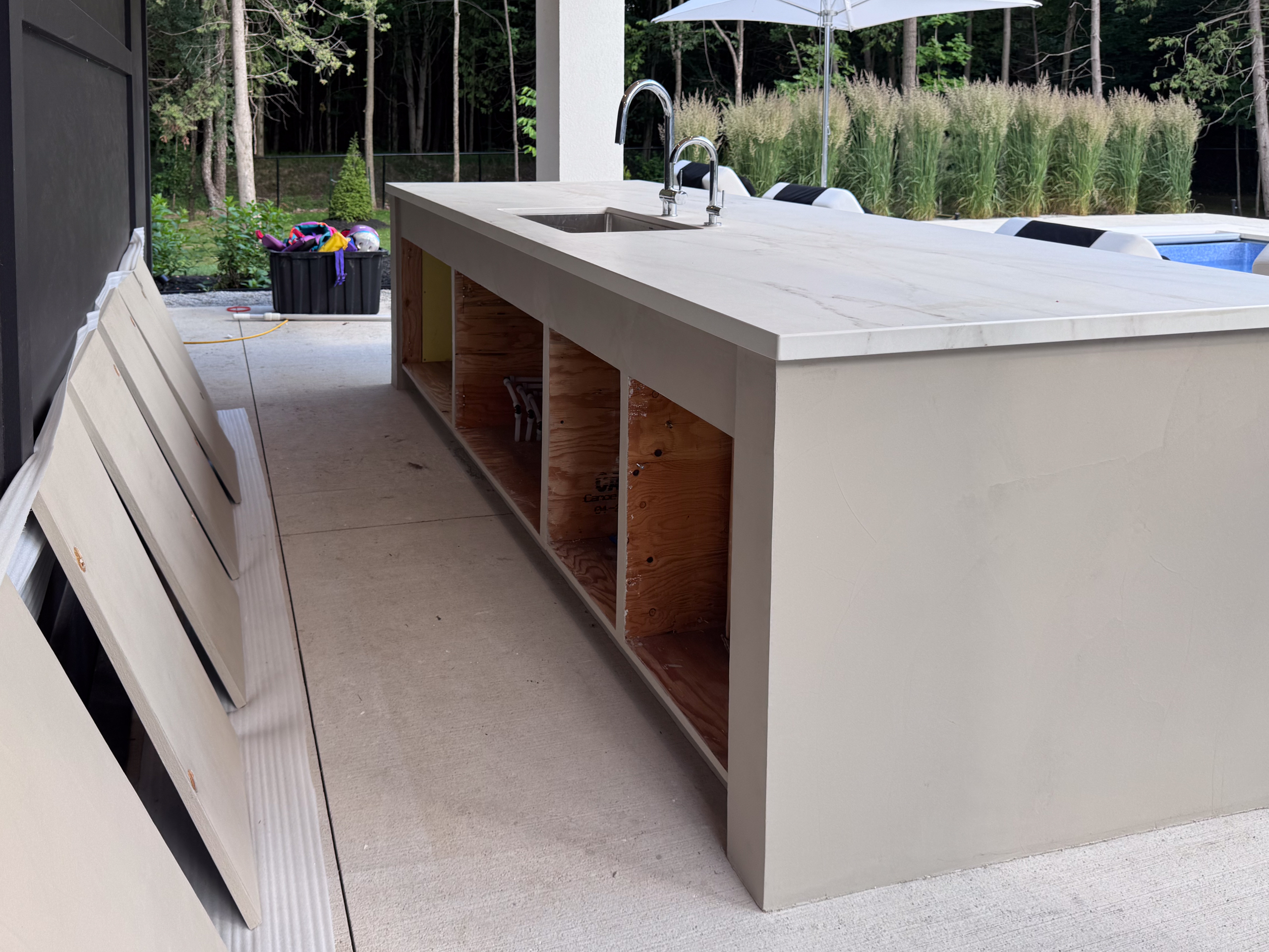 outdoor-microcement-kitchen-cabinet-erin-toronto-2 A luxury modern outdoor kitchen in Erin, Ontario, featuring a seamless greige microcement island with integrated cabinet doors and a sleek porcelain countertop.