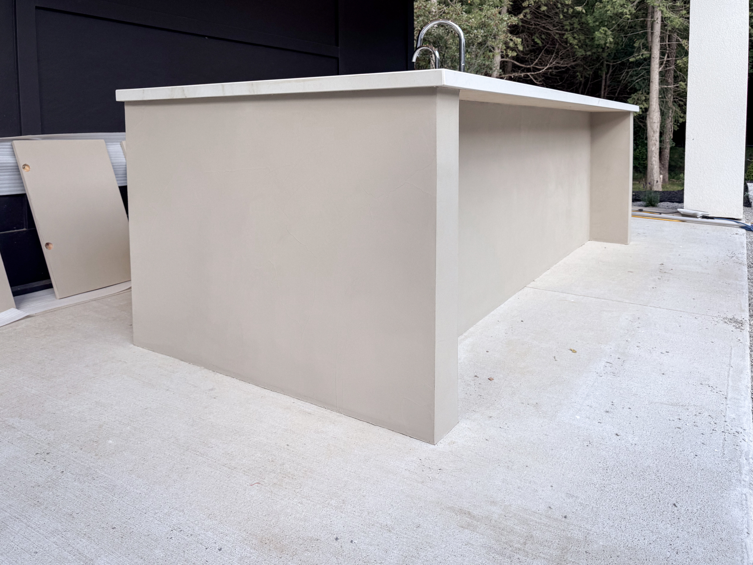 outdoor-microcement-kitchen-cabinet-erin-toronto-3 A luxury modern outdoor kitchen in Erin, Ontario, featuring a seamless greige microcement island with integrated cabinet doors and a sleek porcelain countertop.