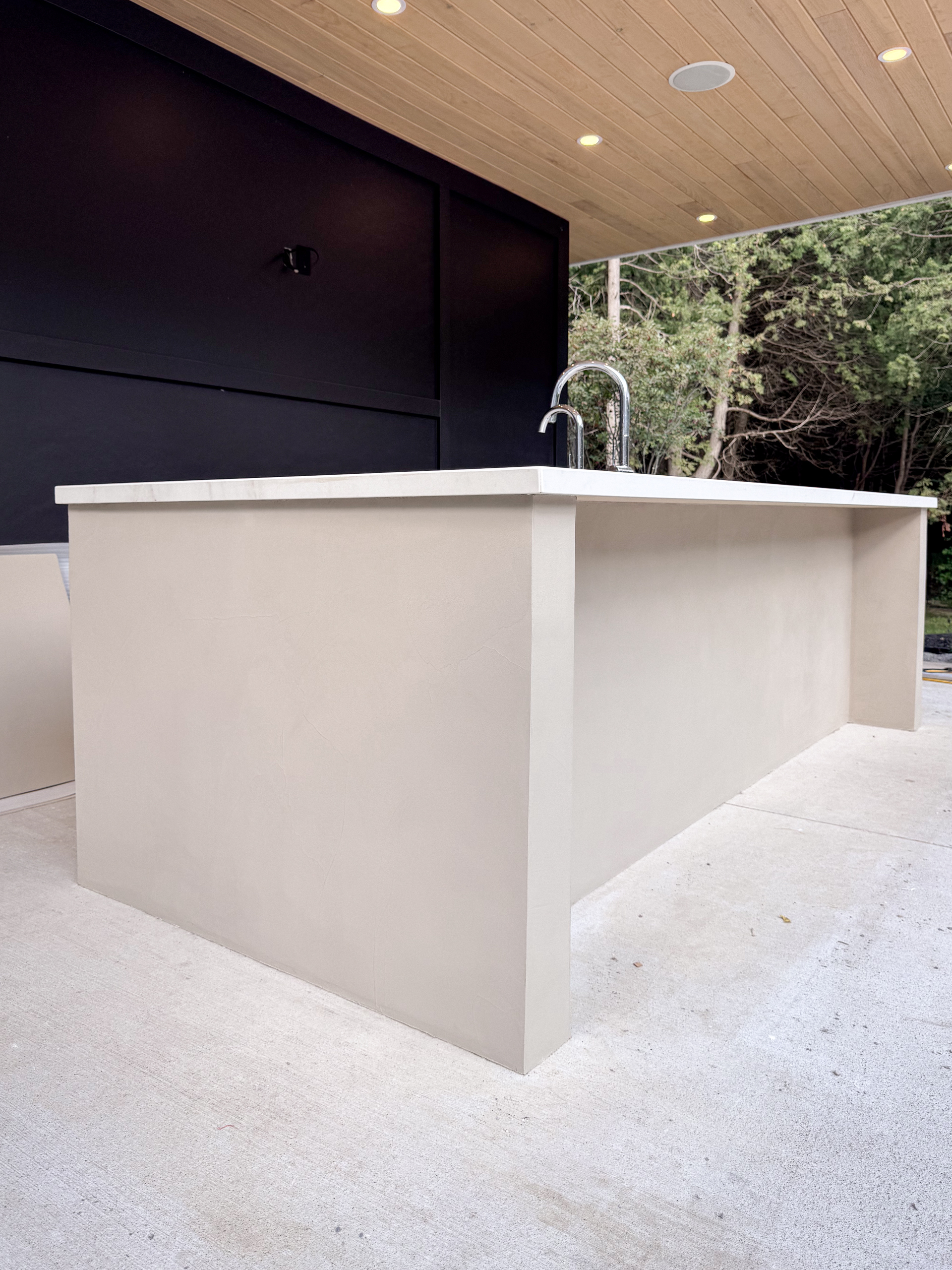 outdoor-microcement-kitchen-cabinet-erin-toronto-4 A luxury modern outdoor kitchen in Erin, Ontario, featuring a seamless greige microcement island with integrated cabinet doors and a sleek porcelain countertop.