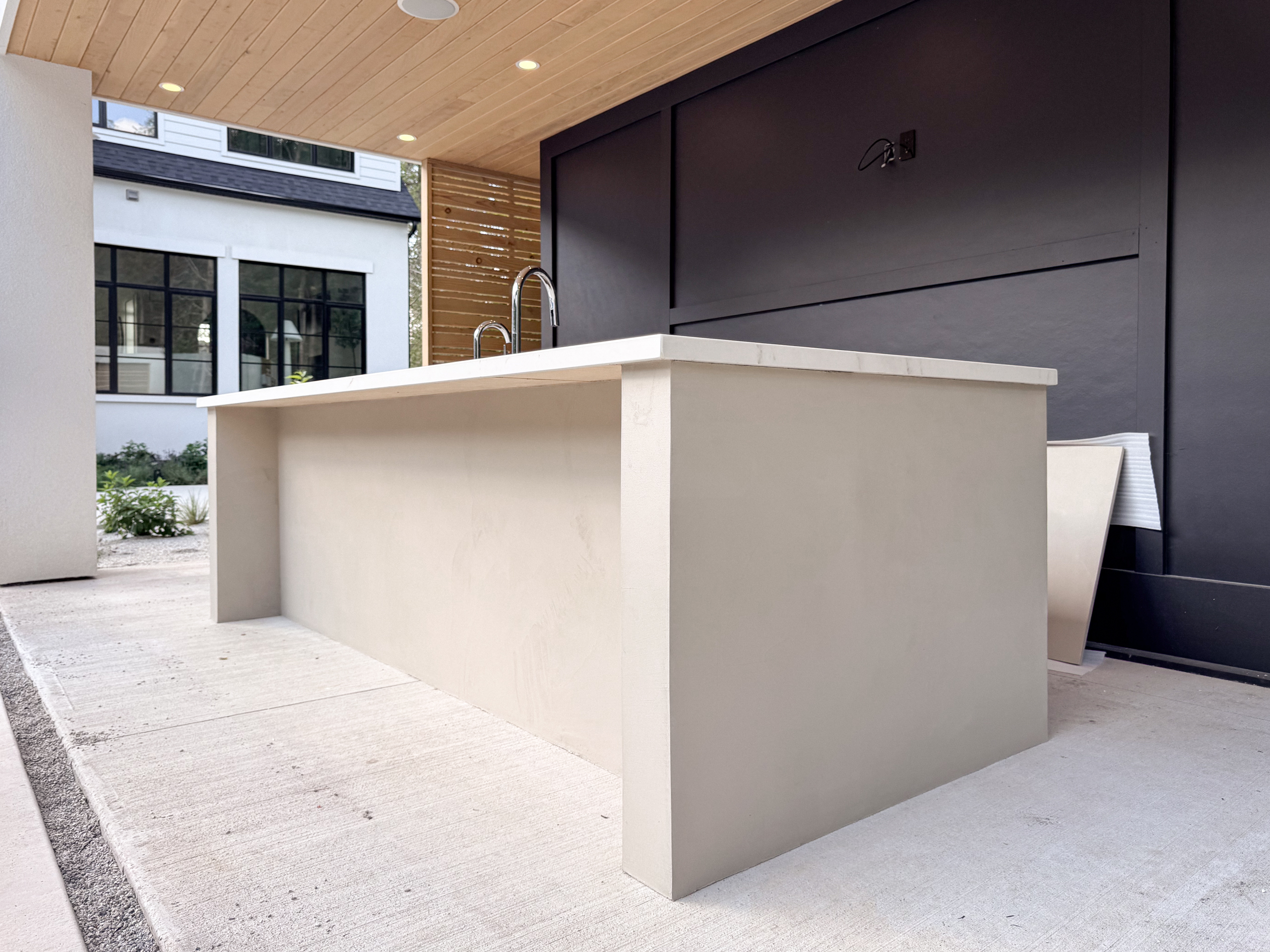 outdoor-microcement-kitchen-cabinet-erin-toronto-6 A luxury modern outdoor kitchen in Erin, Ontario, featuring a seamless greige microcement island with integrated cabinet doors and a sleek porcelain countertop.