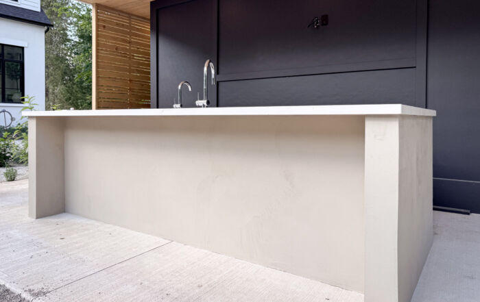 A luxury modern outdoor kitchen in Erin, Ontario, featuring a seamless greige microcement island with integrated cabinet doors and a sleek porcelain countertop.