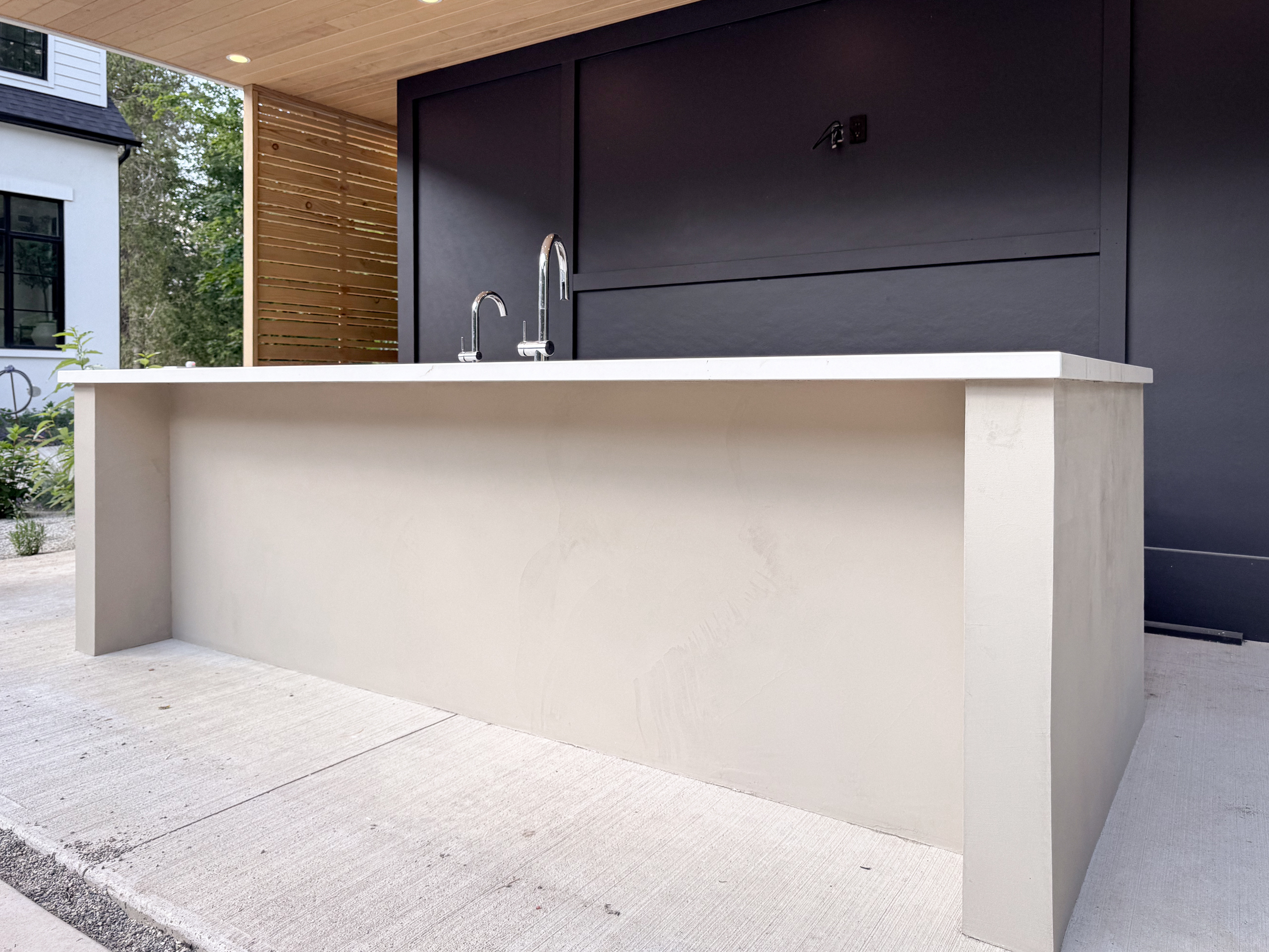 A luxury modern outdoor kitchen in Erin, Ontario, featuring a seamless greige microcement island with integrated cabinet doors and a sleek porcelain countertop.