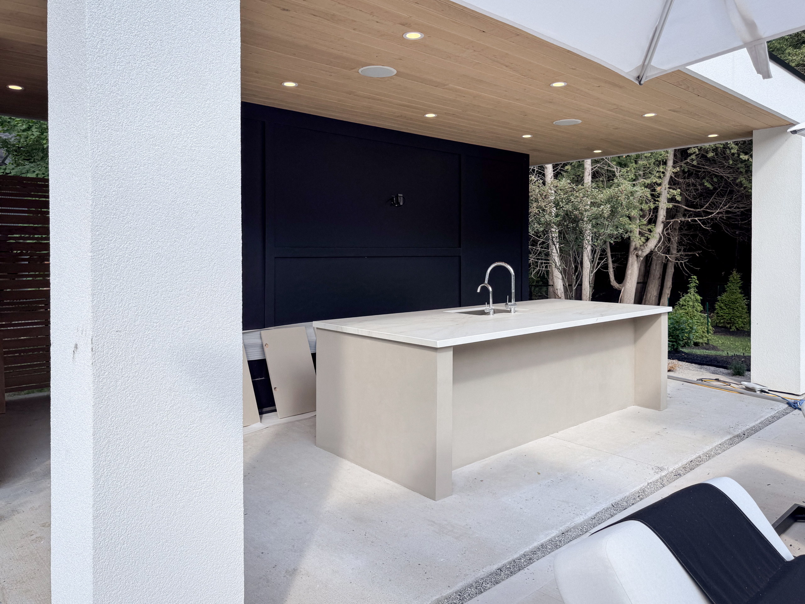 outdoor-microcement-kitchen-cabinet-erin-toronto A luxury modern outdoor kitchen in Erin, Ontario, featuring a seamless greige microcement island with integrated cabinet doors and a sleek porcelain countertop.
