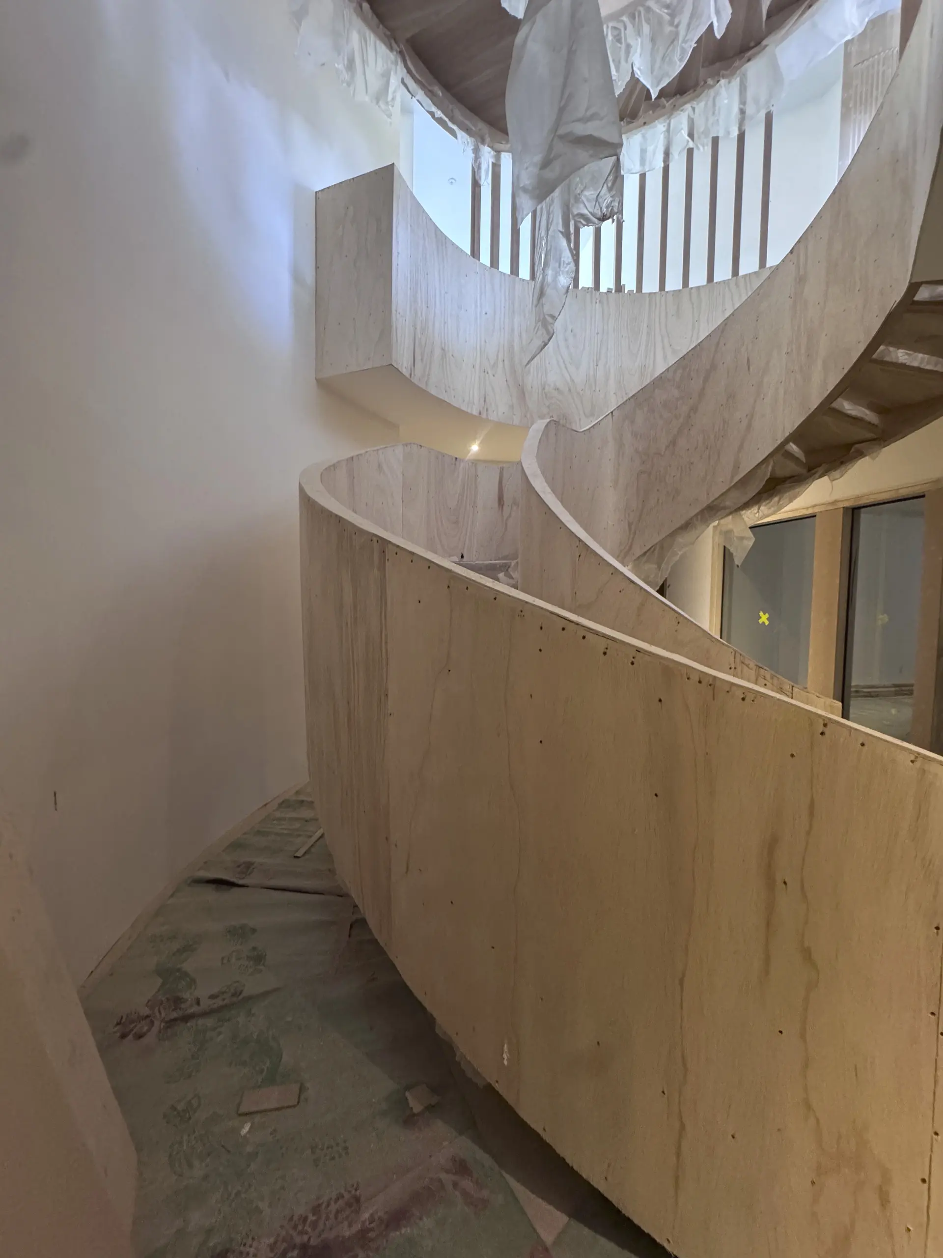 Wide view of a raw MDF spiral staircase skirt before microcement preparation in a Richmond Hill home.