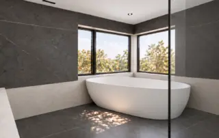 Freestanding tub beside charcoal shower walls and light greige microcement surfaces in a North York bathroom.