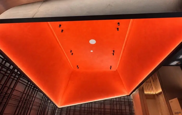 Wide view of a finished red limewash dropped ceiling, with the ceiling plane framed by dark wall detailing and warm wood in a Toronto restaurant interior.