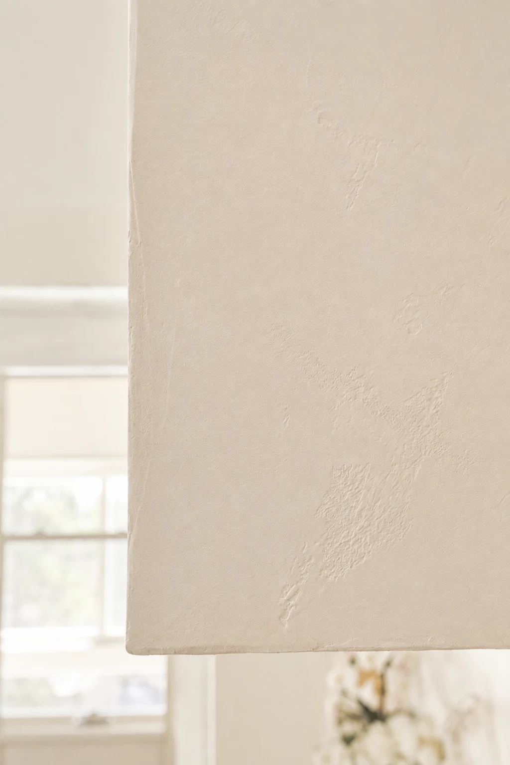 Close-up of a light-toned plaster hood surface with fine texture and gentle variations in reflected light.