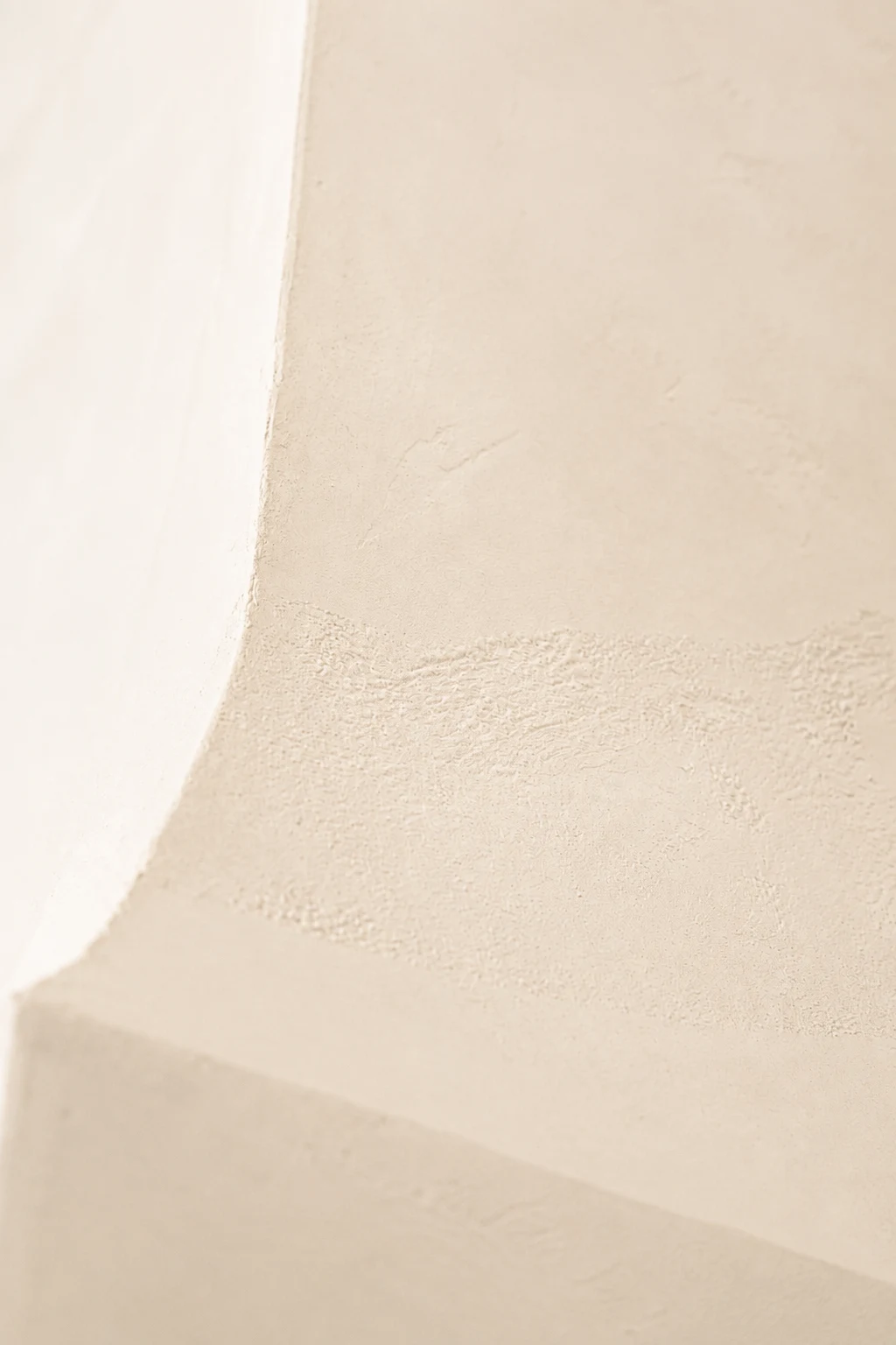 Close view of a pale plaster range hood, showing its curved transition and softly textured surface.